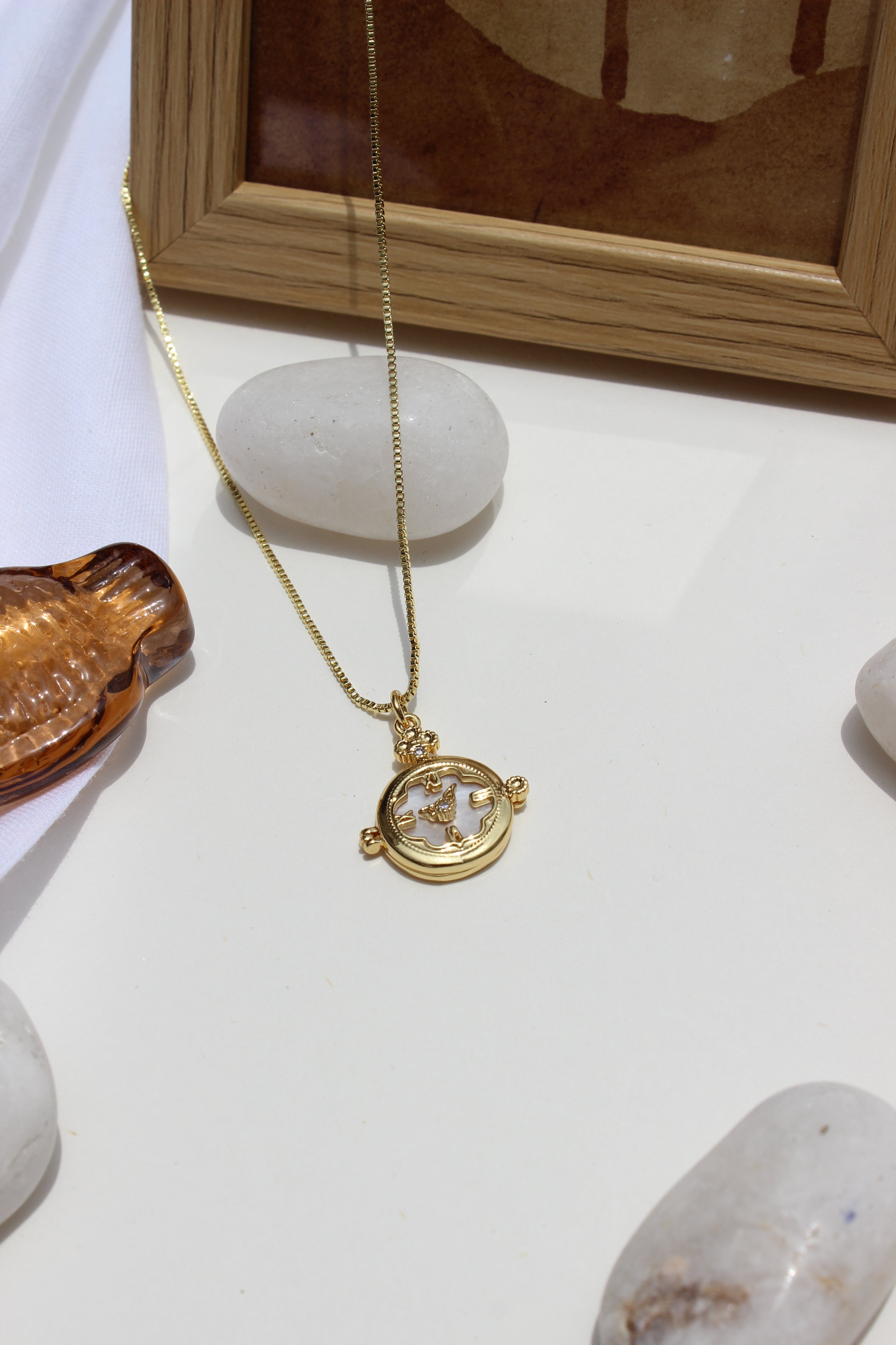 Whitespell Pendant Necklace on a wooden frame around the stones and seashell