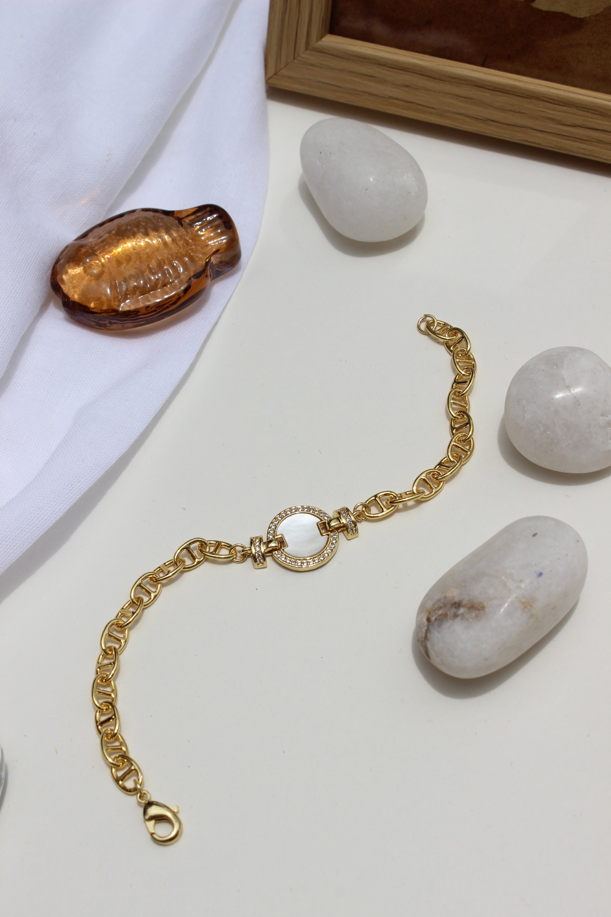 Sea of Light Bracelet on a white surface with stones and a wooden frame in the background