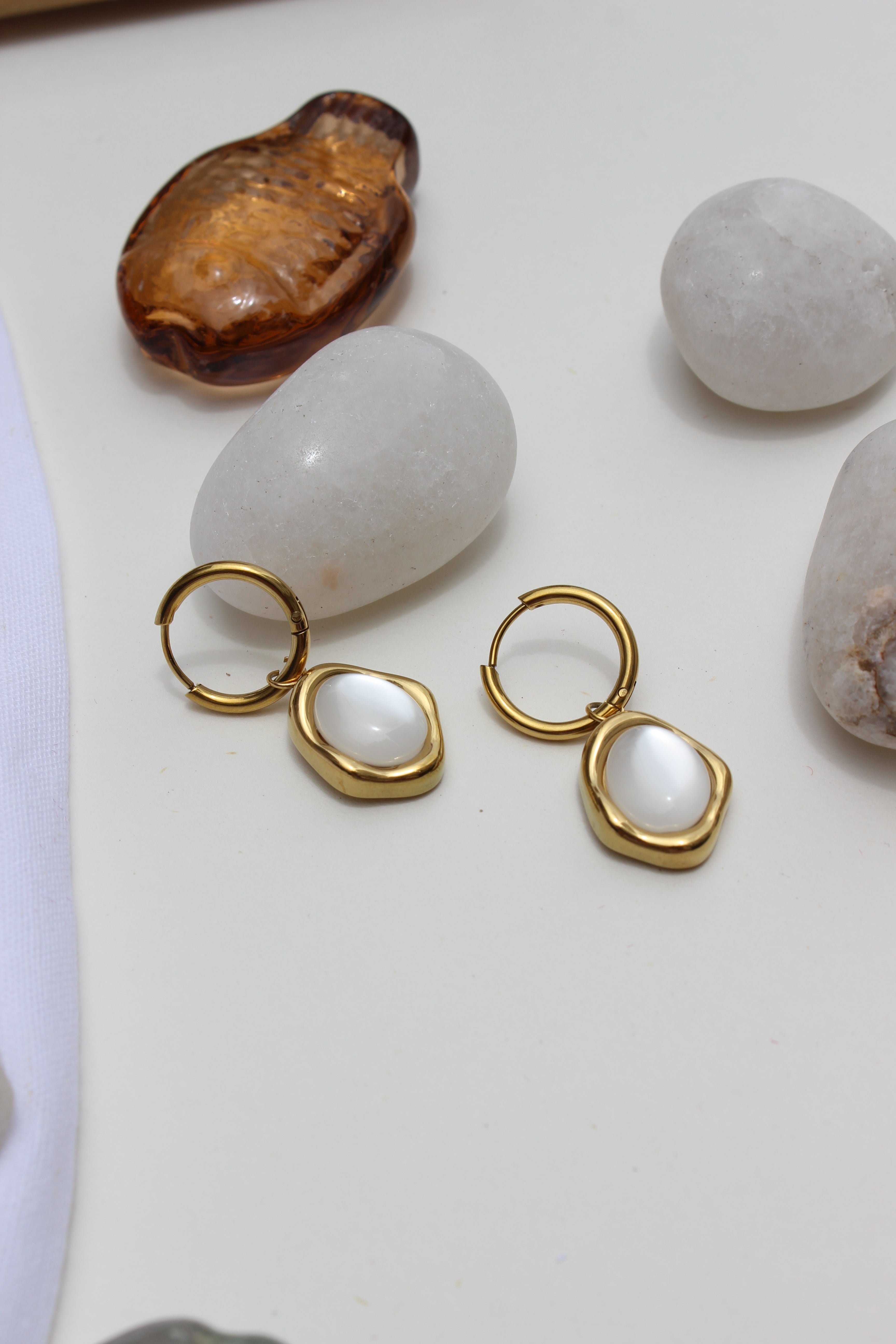 Stillwater Pearl Hoop Earrings with white stones on a light surface with stones around