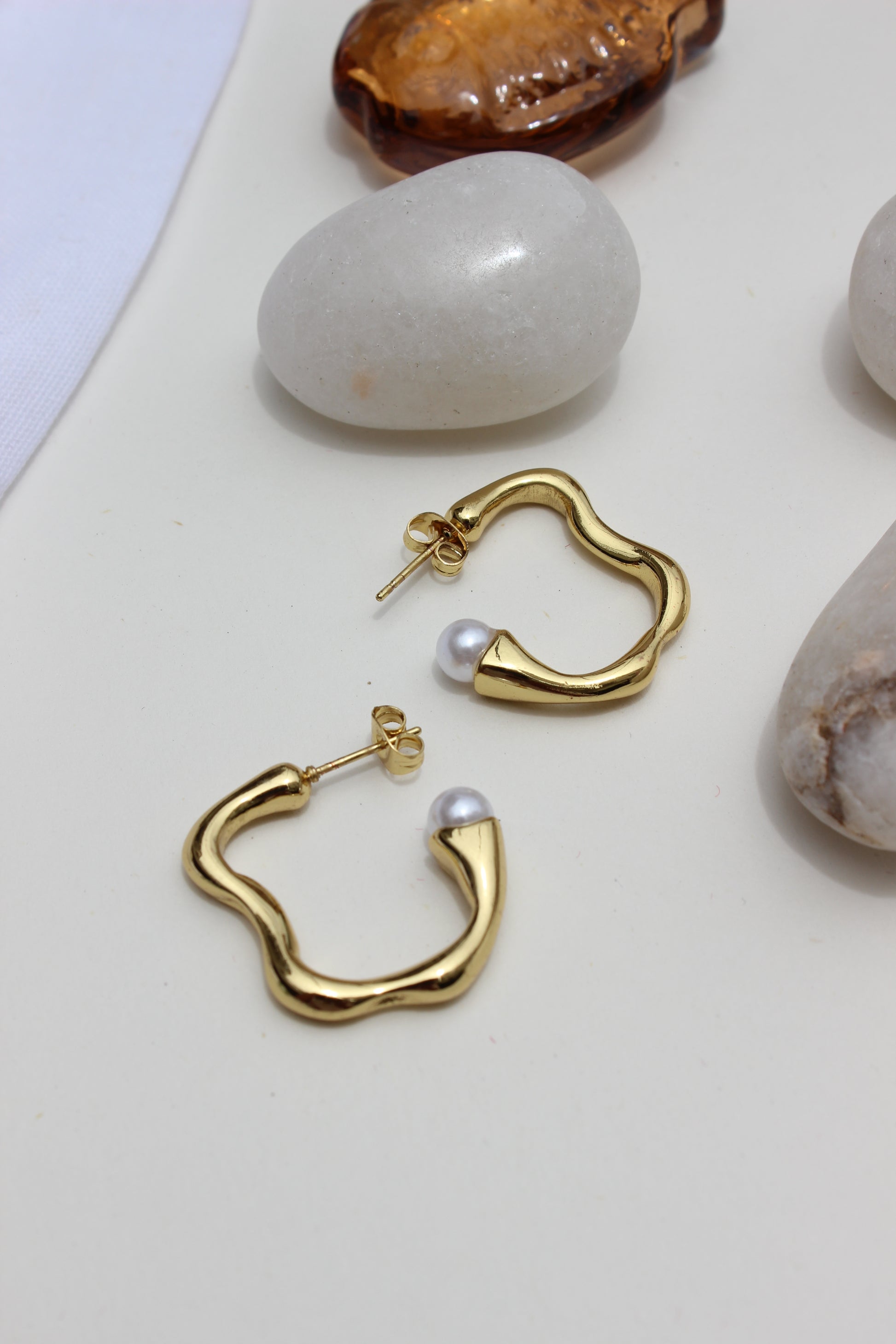 Pearl Fold Half Hoop Earrings on a light surface with stones