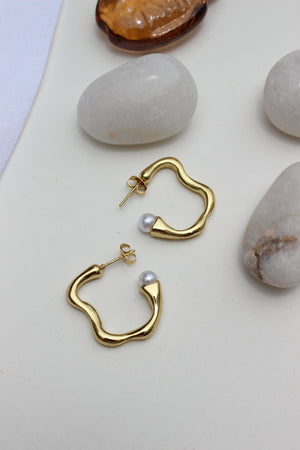 Pearl Fold Half Hoop Earrings on a light surface with stones in the background