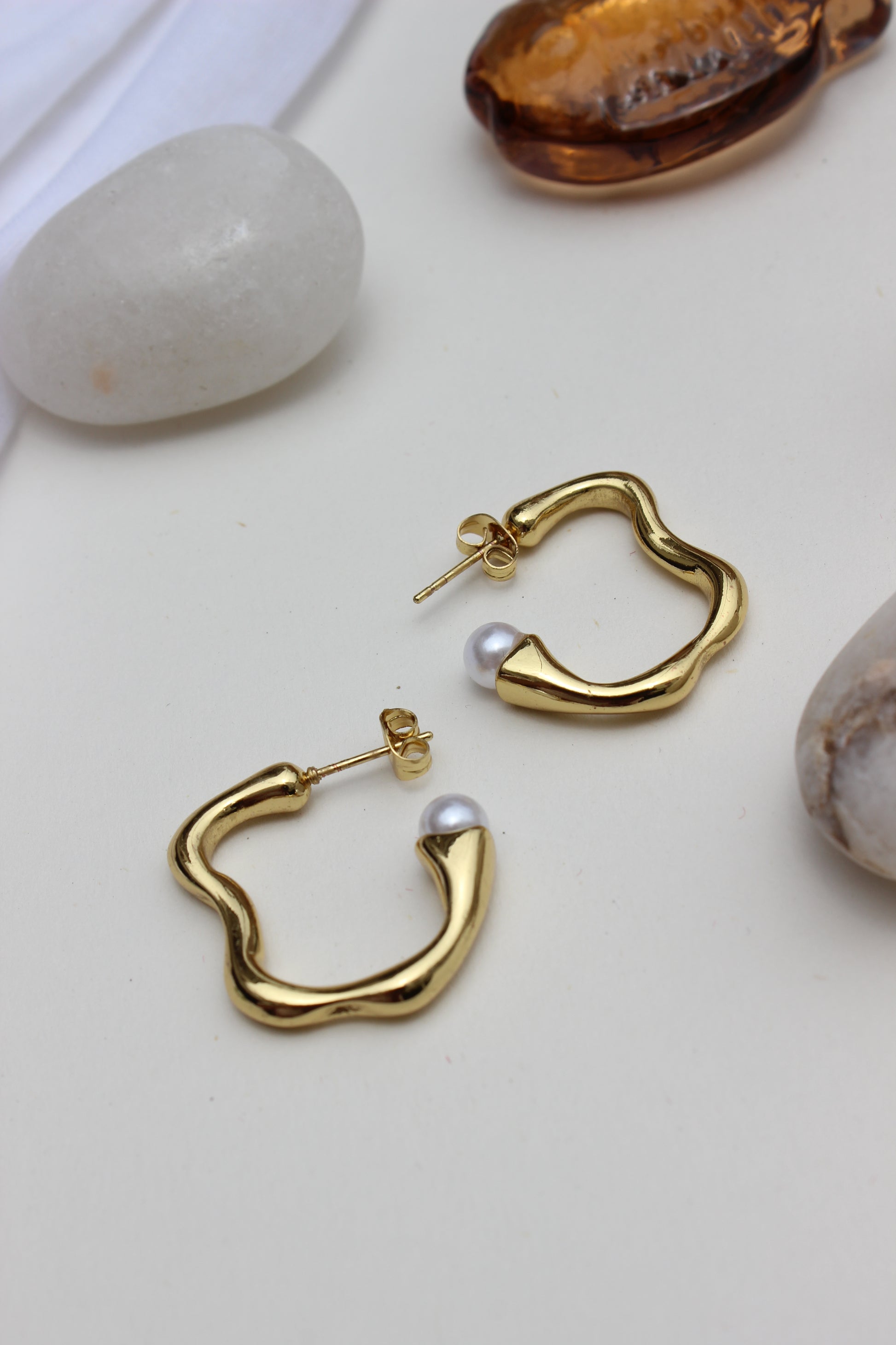 Pearl Fold Half Hoop Earrings on a white surface with seashells