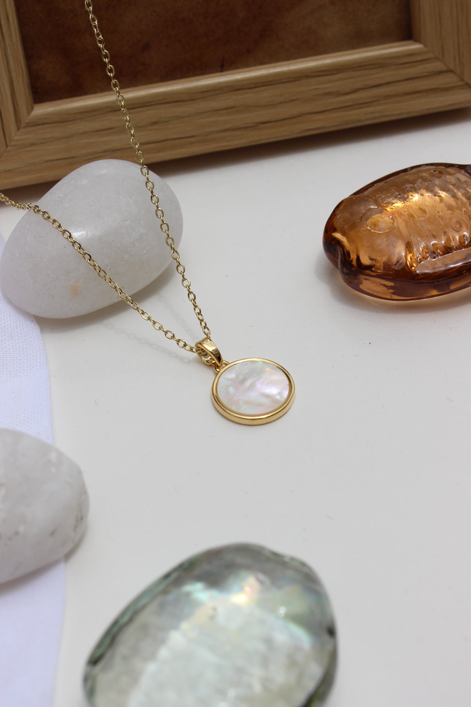 Melted Calm Pendant Necklace on a white surface with stones and a frame