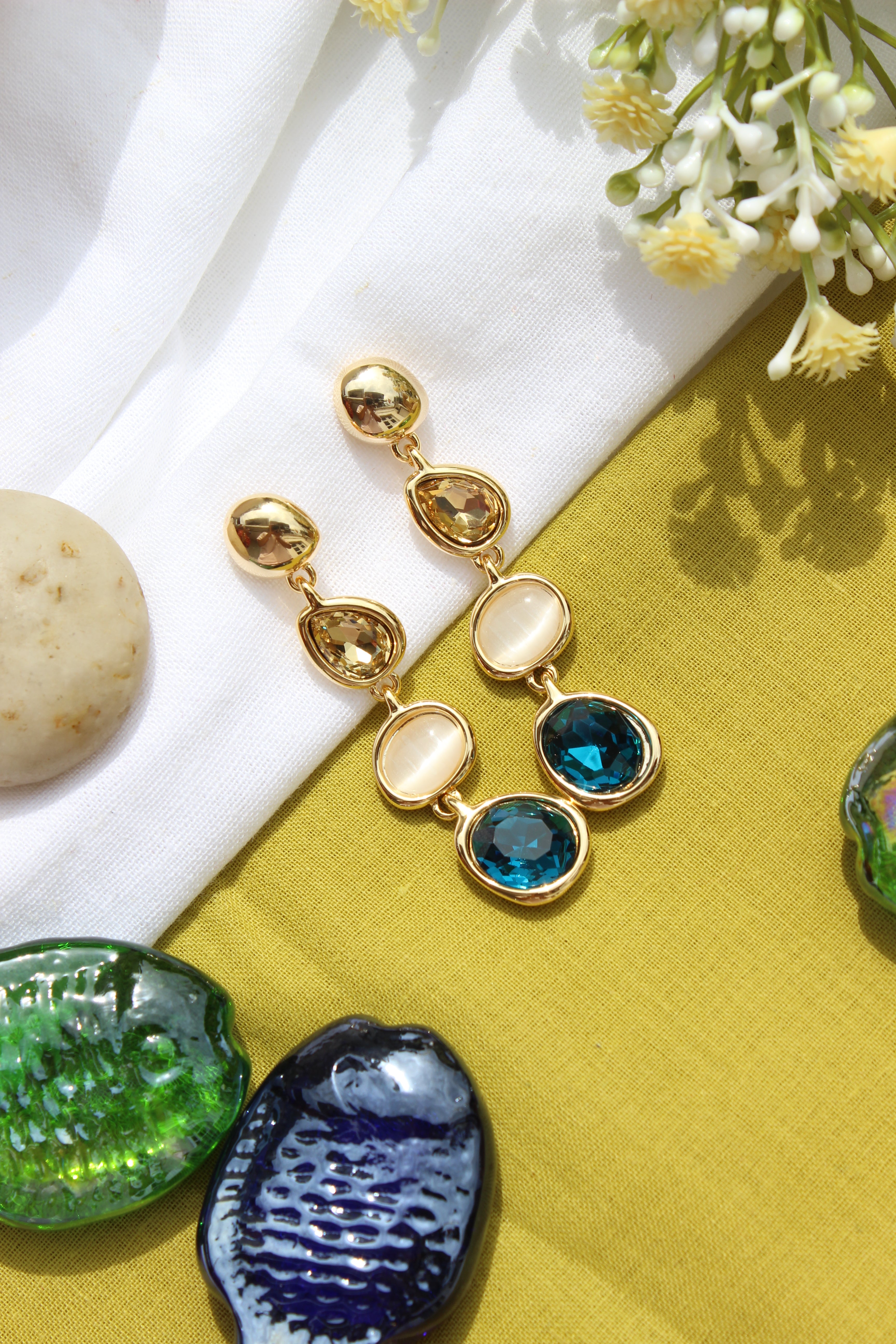 Blueberry Flame Earrings on a yellow fabric background with decorative stones and seashells