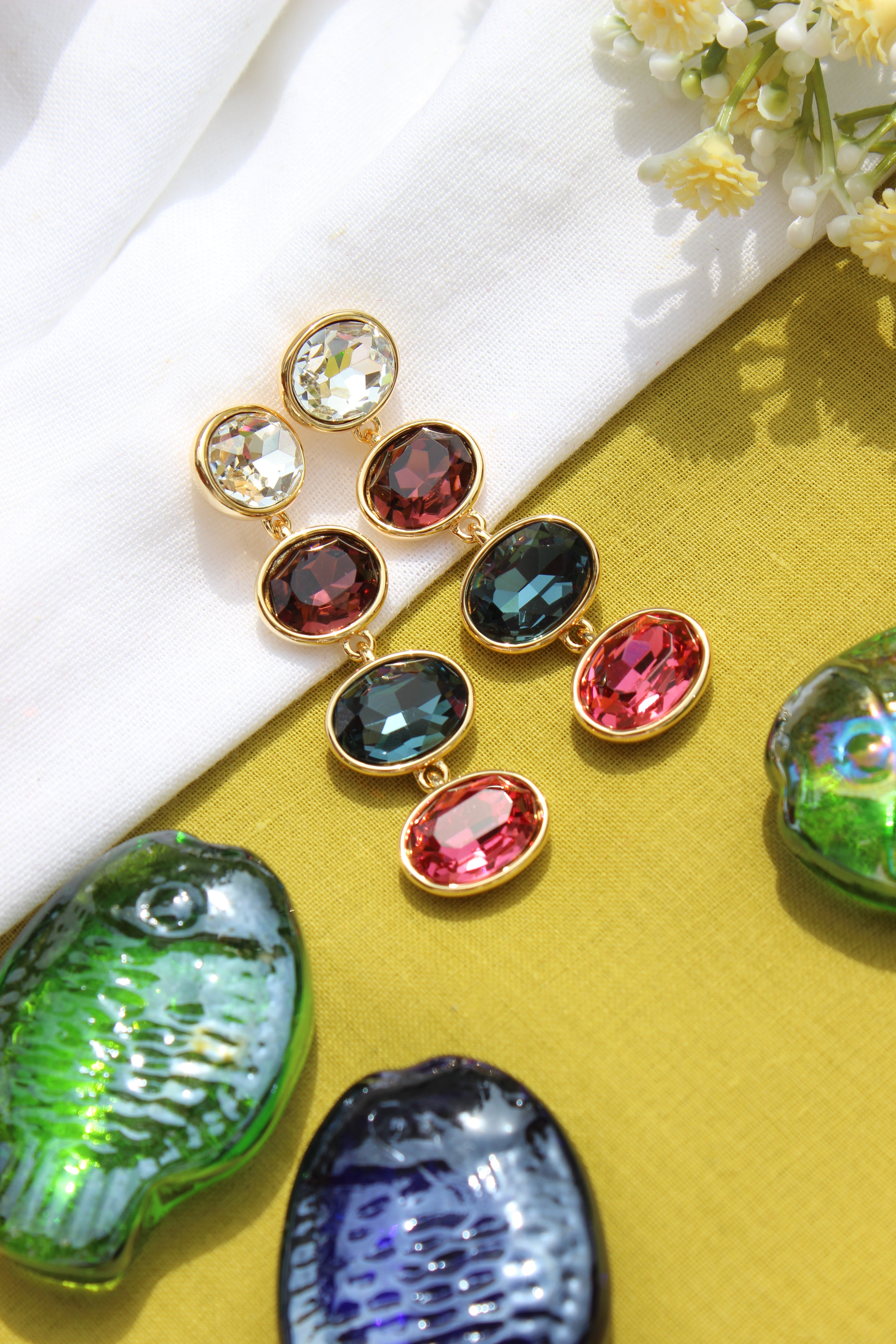 Aura Drape Earrings on a textured surface with flowers and shells