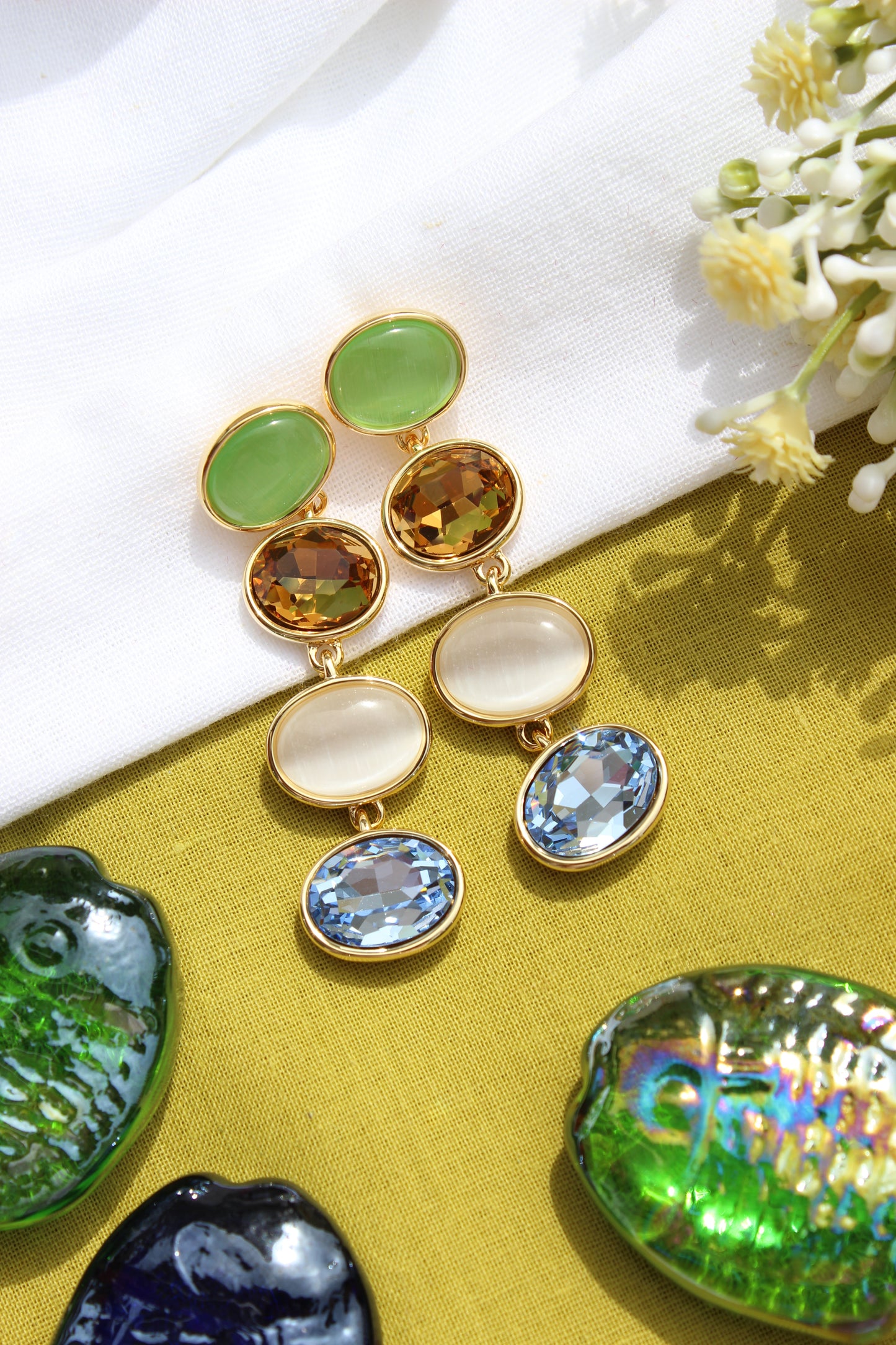 Gemstone Reverie Earrings on a textured surface with flowers and shells in the background