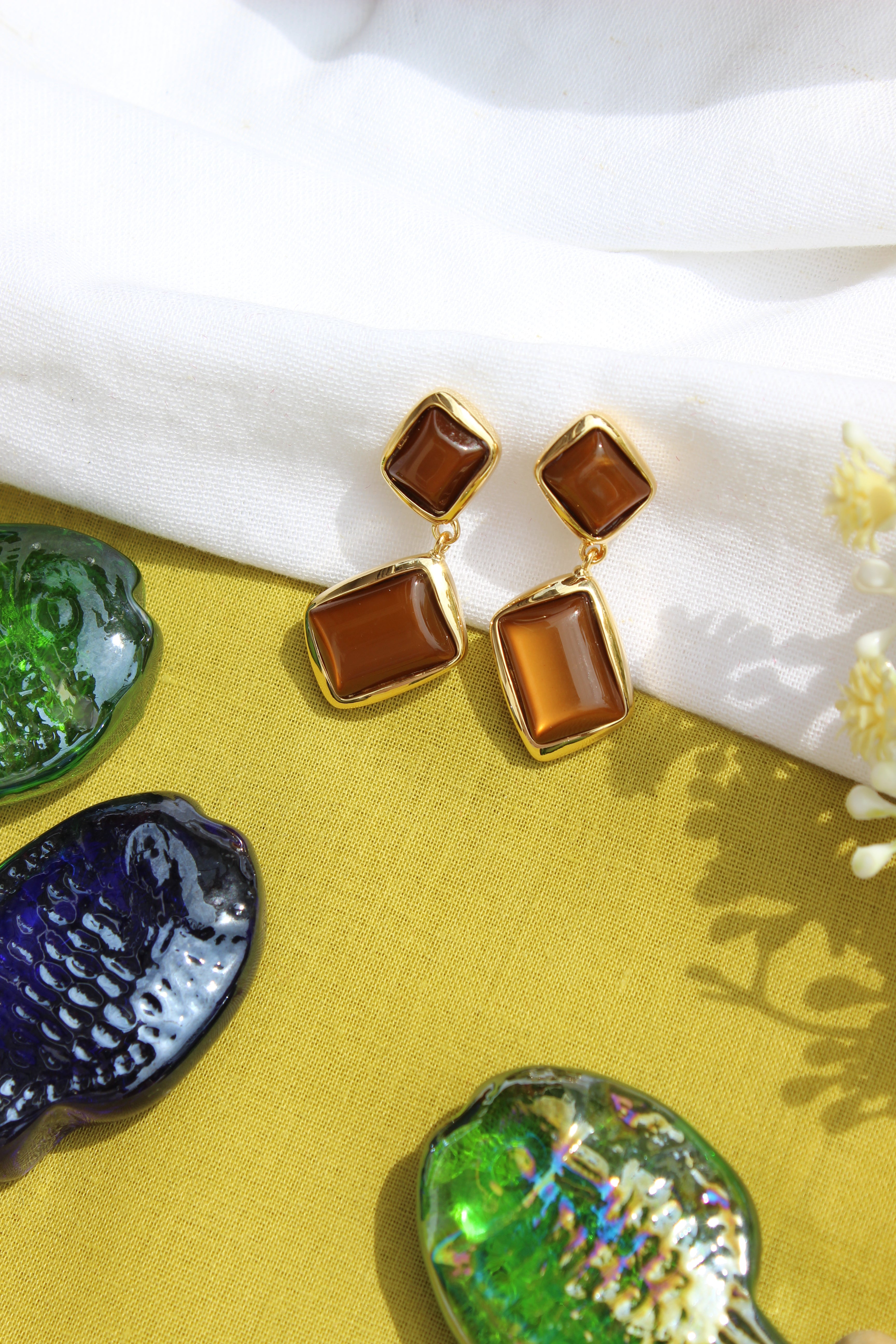 Amber Dust Earrings on a yellow surface with decorative shells