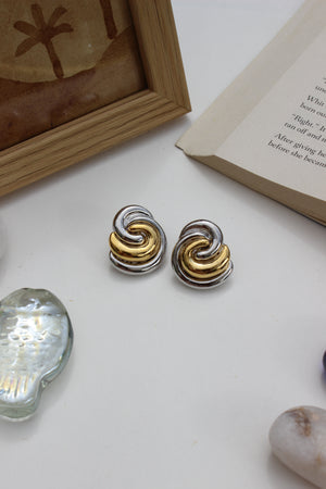Yin-Yang stud earrings in gold and silver on white surface with open book and seashell