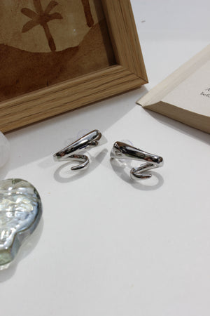 Midnight Curve Earrings on a white surface with a wooden frame and crystal seashell in the background