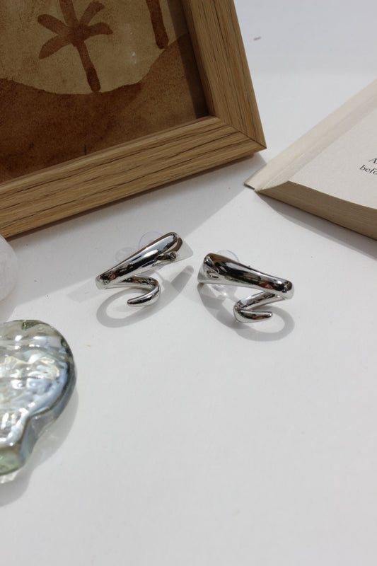Midnight Curve Earrings on a white surface with a wooden frame and crystal seashell in the background