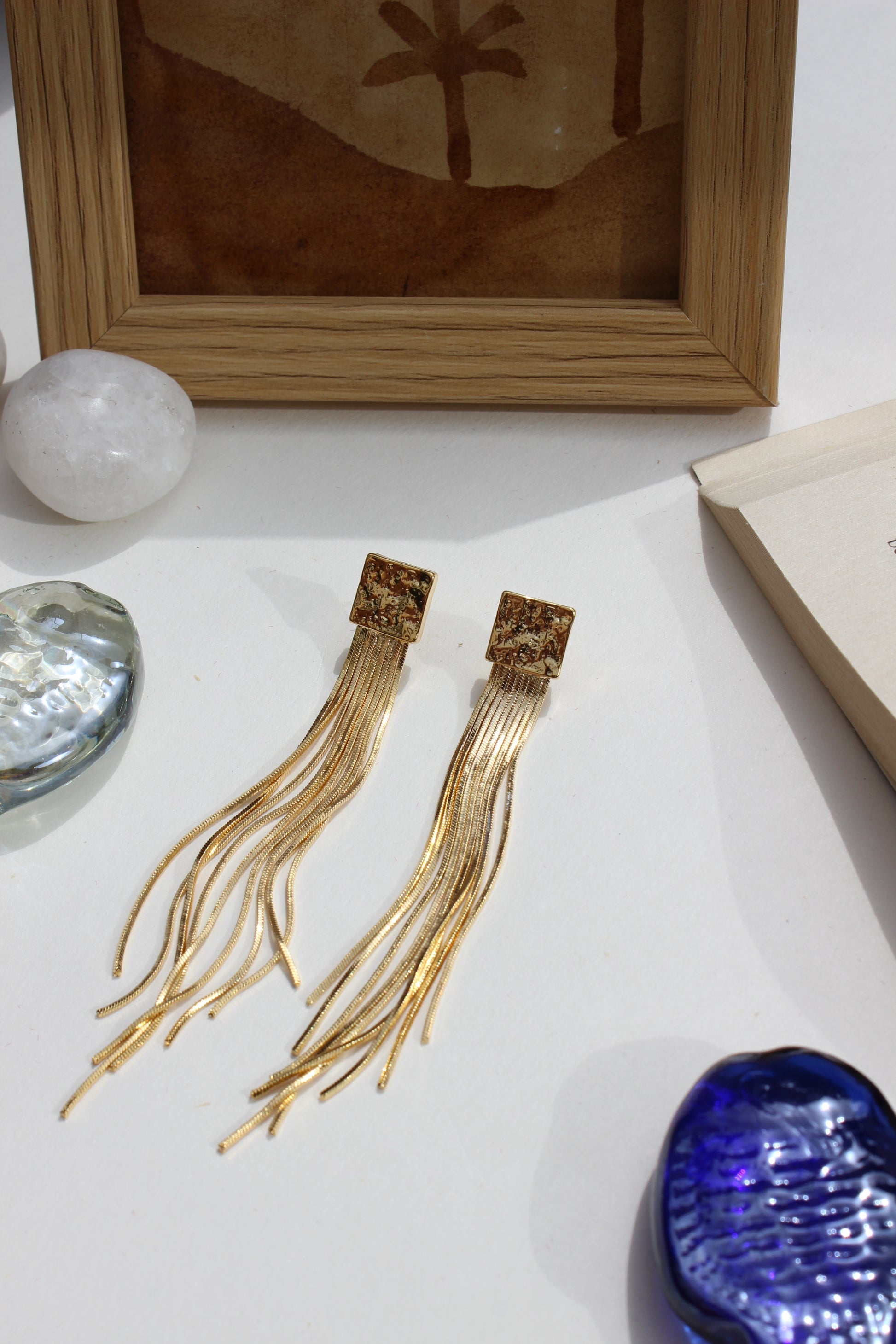 Soft Steel Earrings on a white surface with a wooden frame and decorative stones