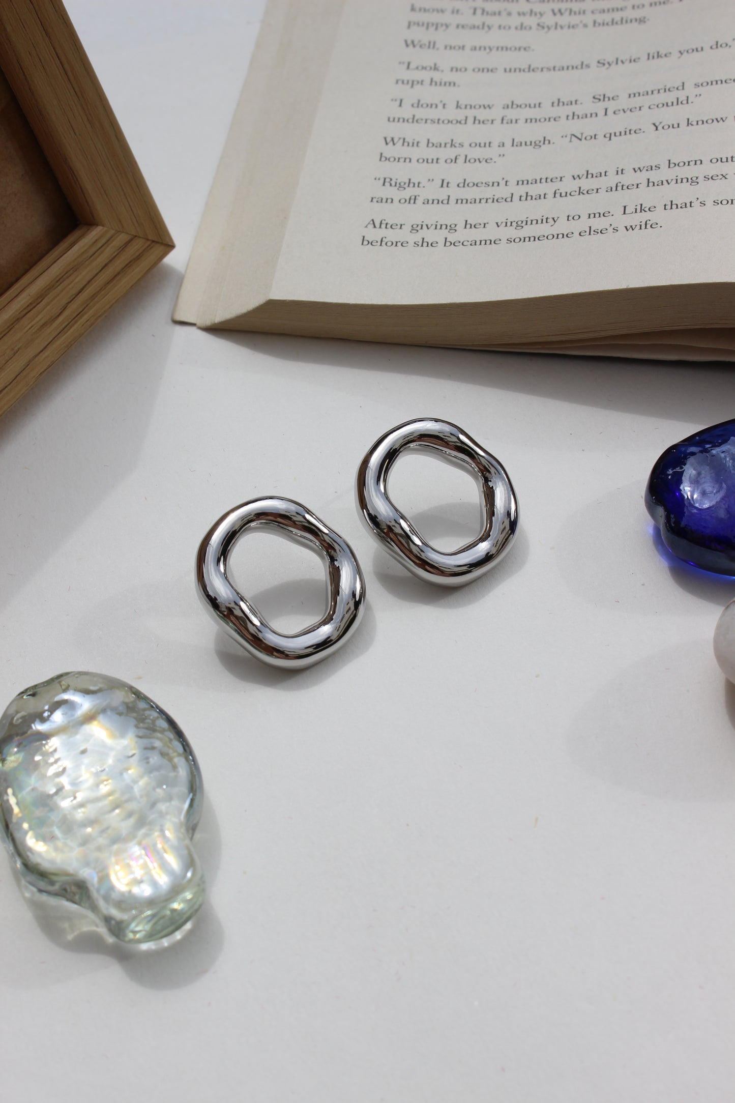 Lucid Frost Earrings on a white surface with a book and seashell in the background