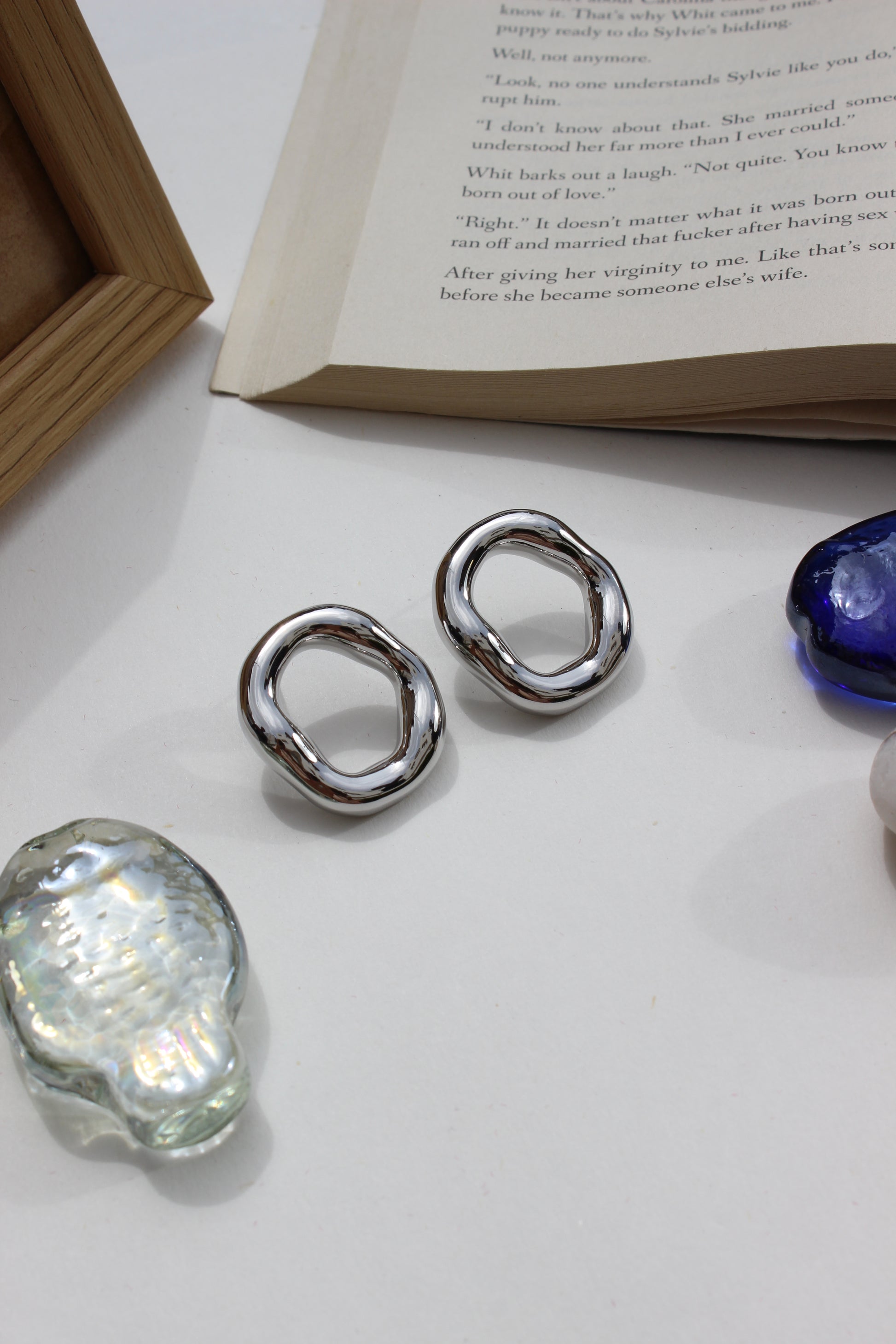 Lucid Frost Earrings on a white surface with a book and seashell in the background