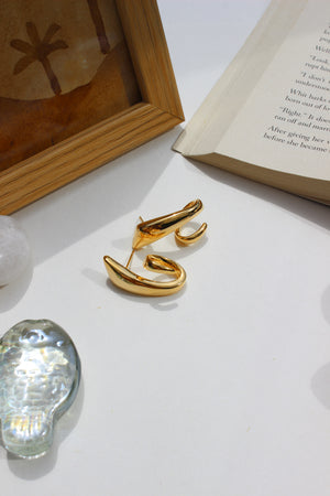 Fierce Gleam Earrings on a white surface with a book and crystal seashell in the background