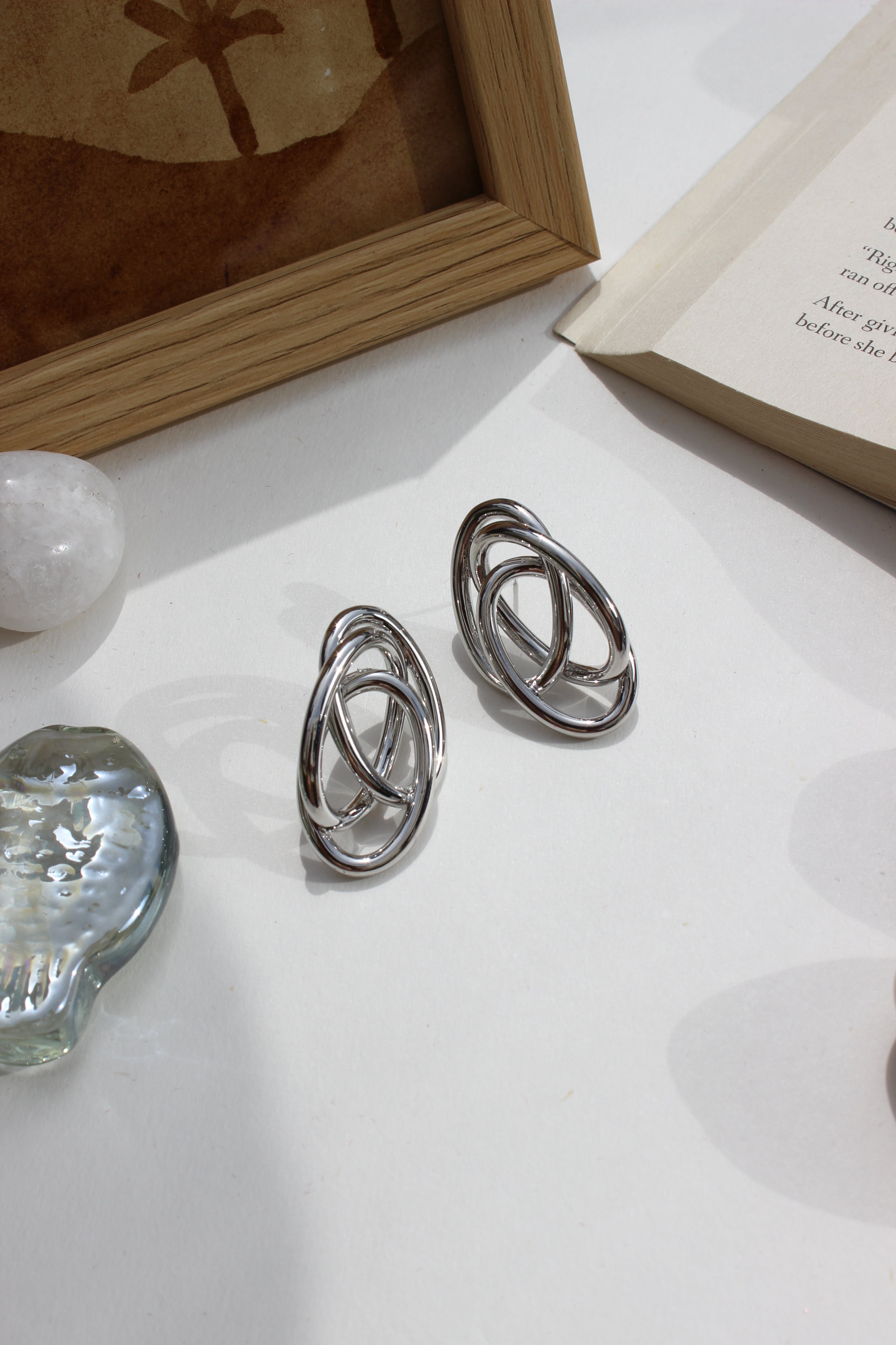 Silver Orbit Earrings on a white surface with a book and decorative items in the background