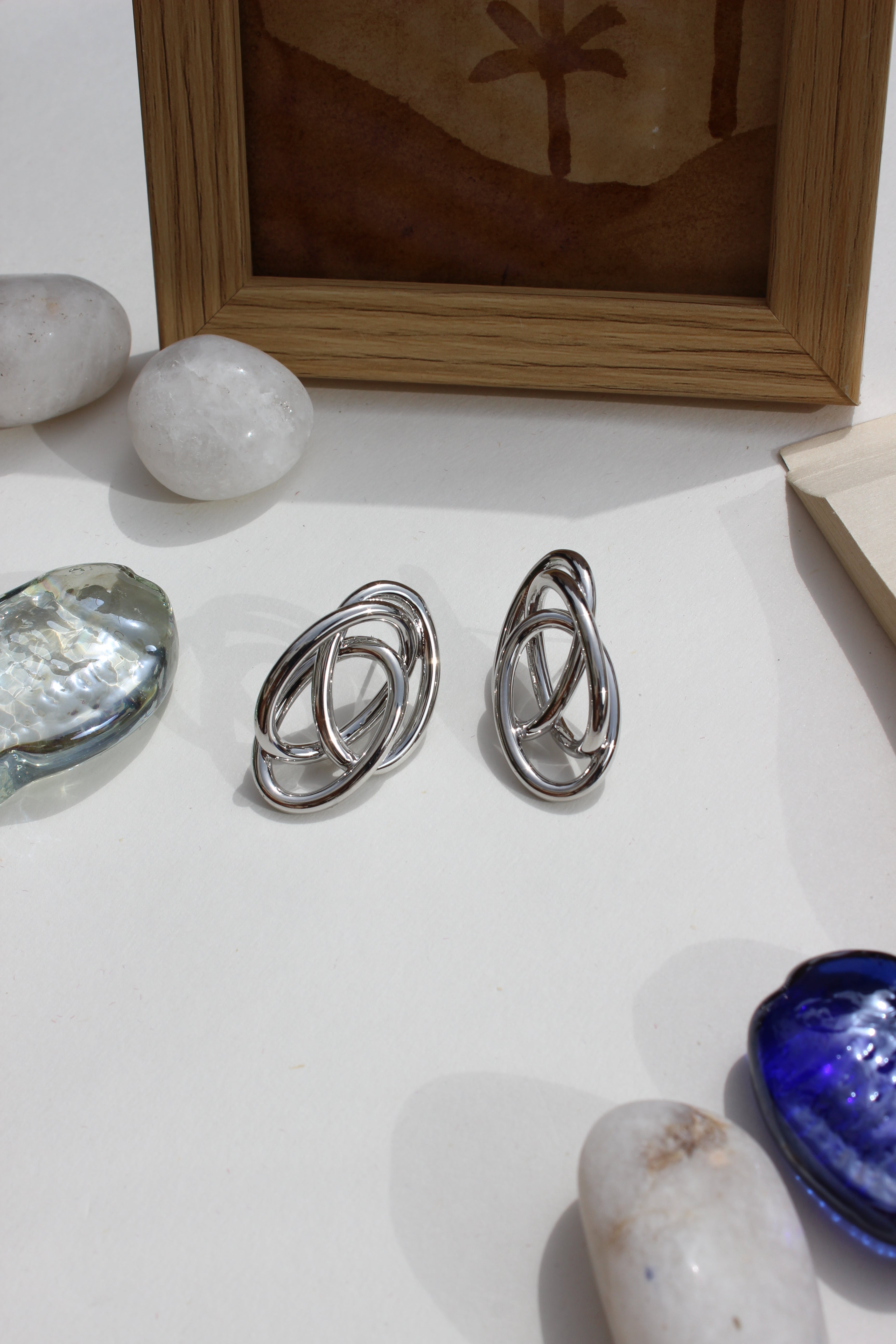 Silver Orbit Earrings on a white surface with a framed artwork and other objects