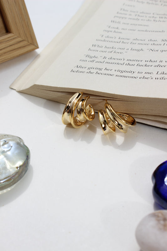 Solar Grip Earrings on an open book with a shell and blue object in the background