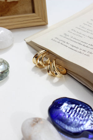 Solar Grip Earrings on an open book with a blue shell and framed picture in the background
