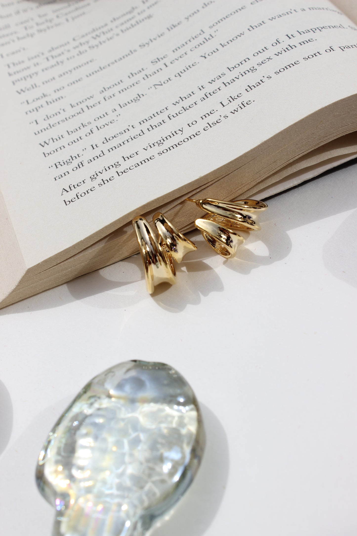 Solar Grip Earrings on an open book with a crystal seashell nearby