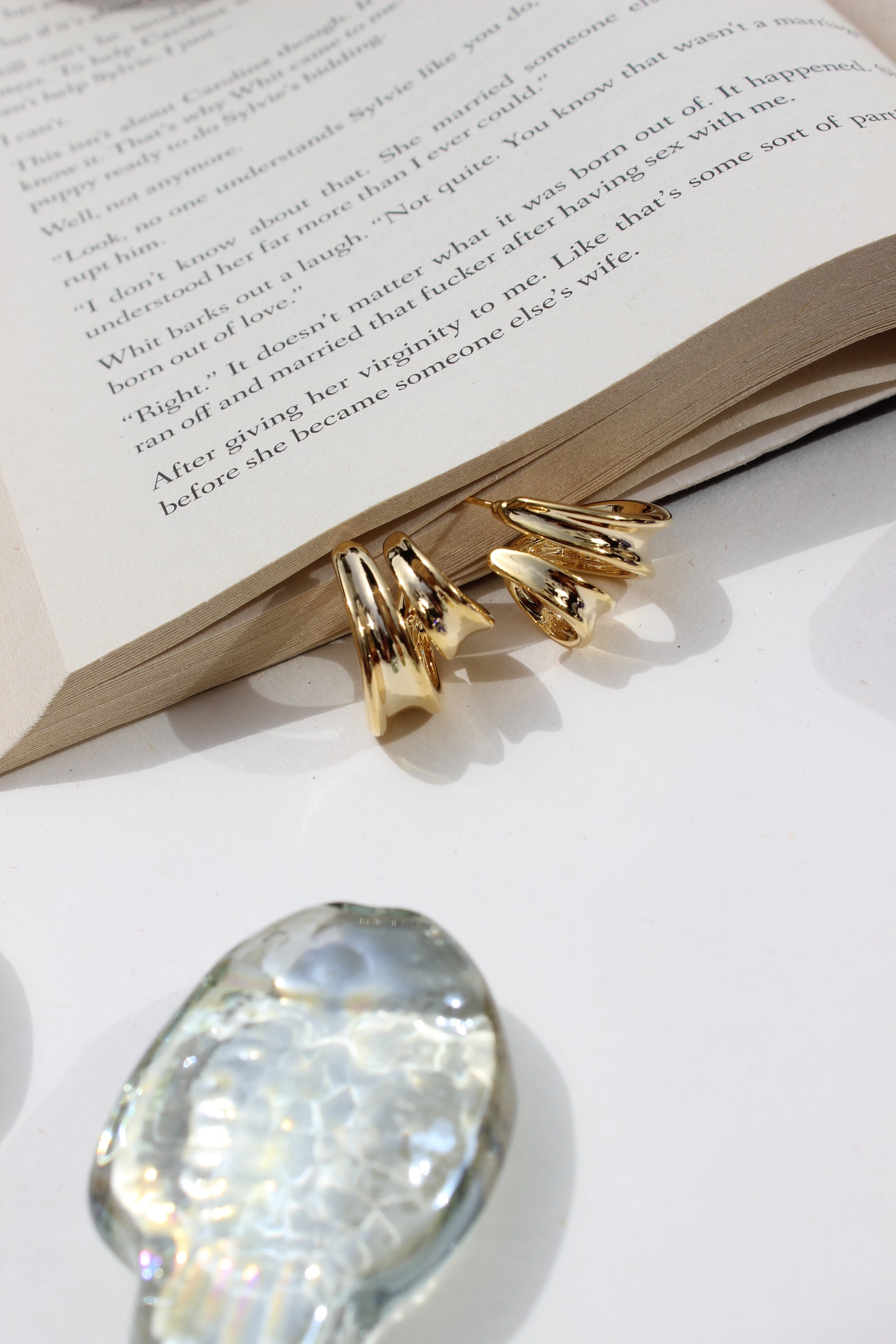 Solar Grip Earrings on an open book with a crystal seashell nearby