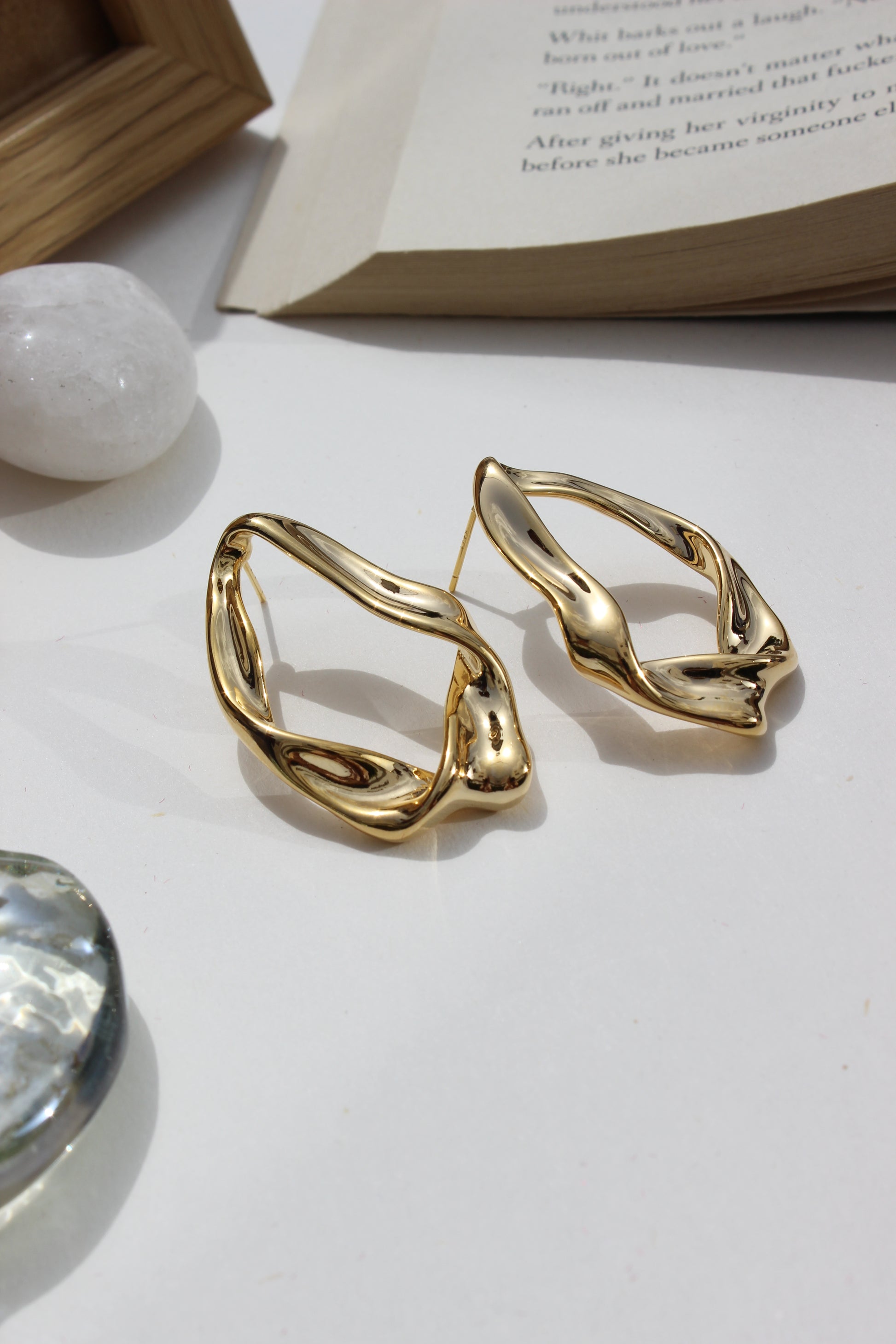 Golden Hug Earrings on a white surface with a blurred book and crystal in the background