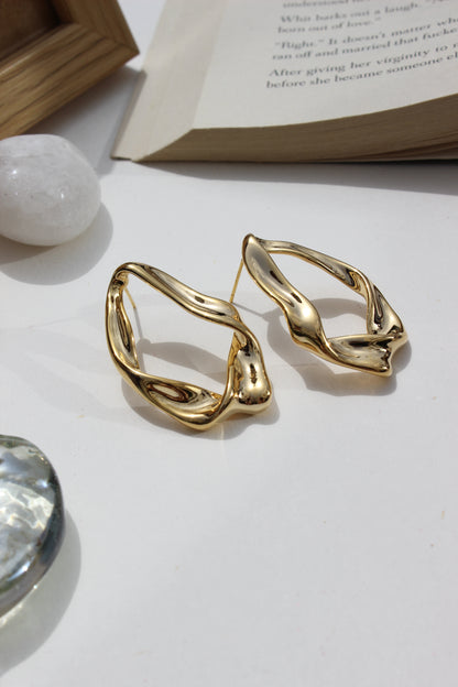 Golden Hug Earrings on a white surface with a blurred book and crystal in the background