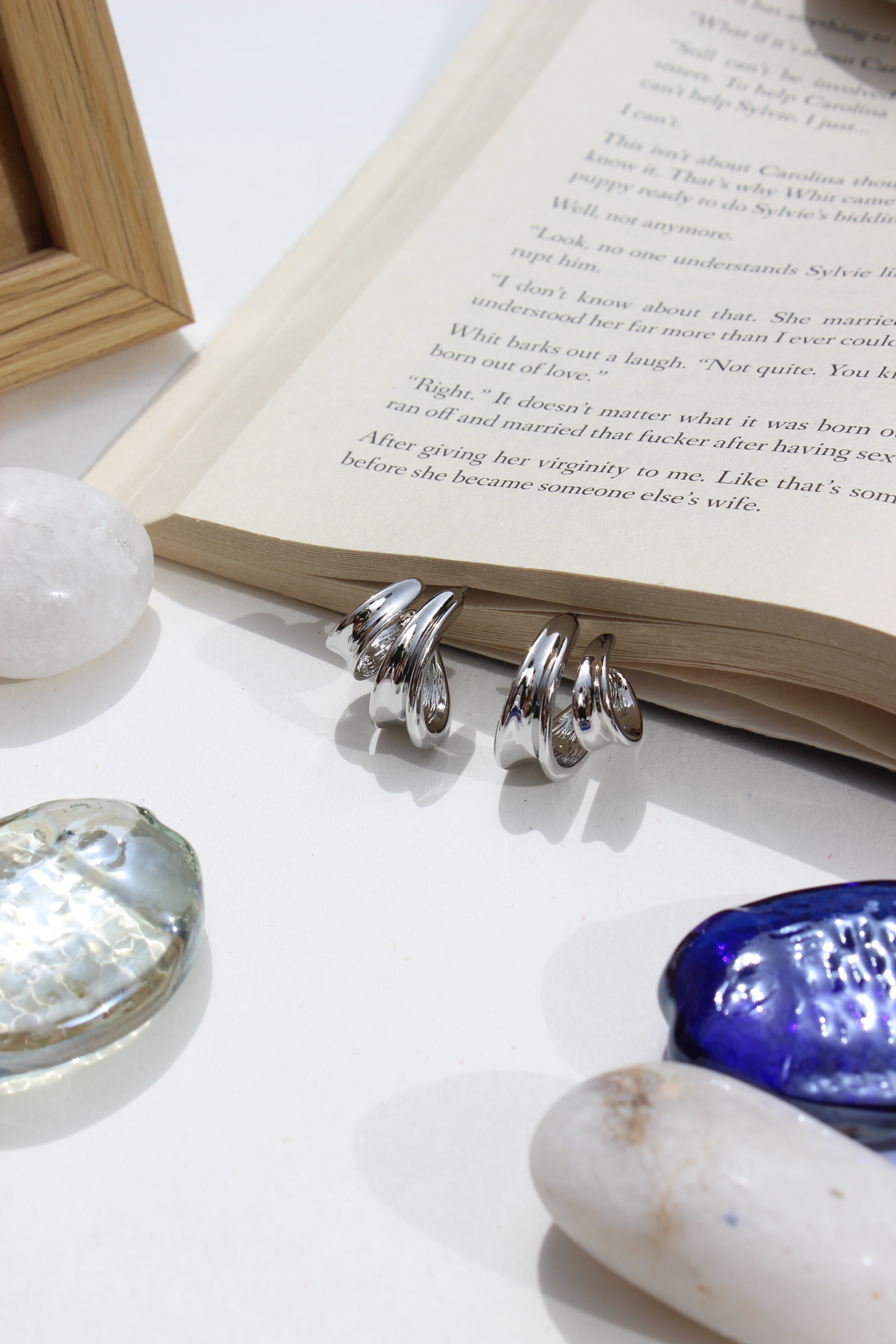 Seasonal Winter Hug Earrings hanging on open book with decorative sea shells, festive jewellery for women, white background