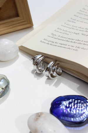 Affordable Winter Hug Earrings displayed on book pages surrounded by sea shells, cozy winter jewellery gift for her, white backdrop