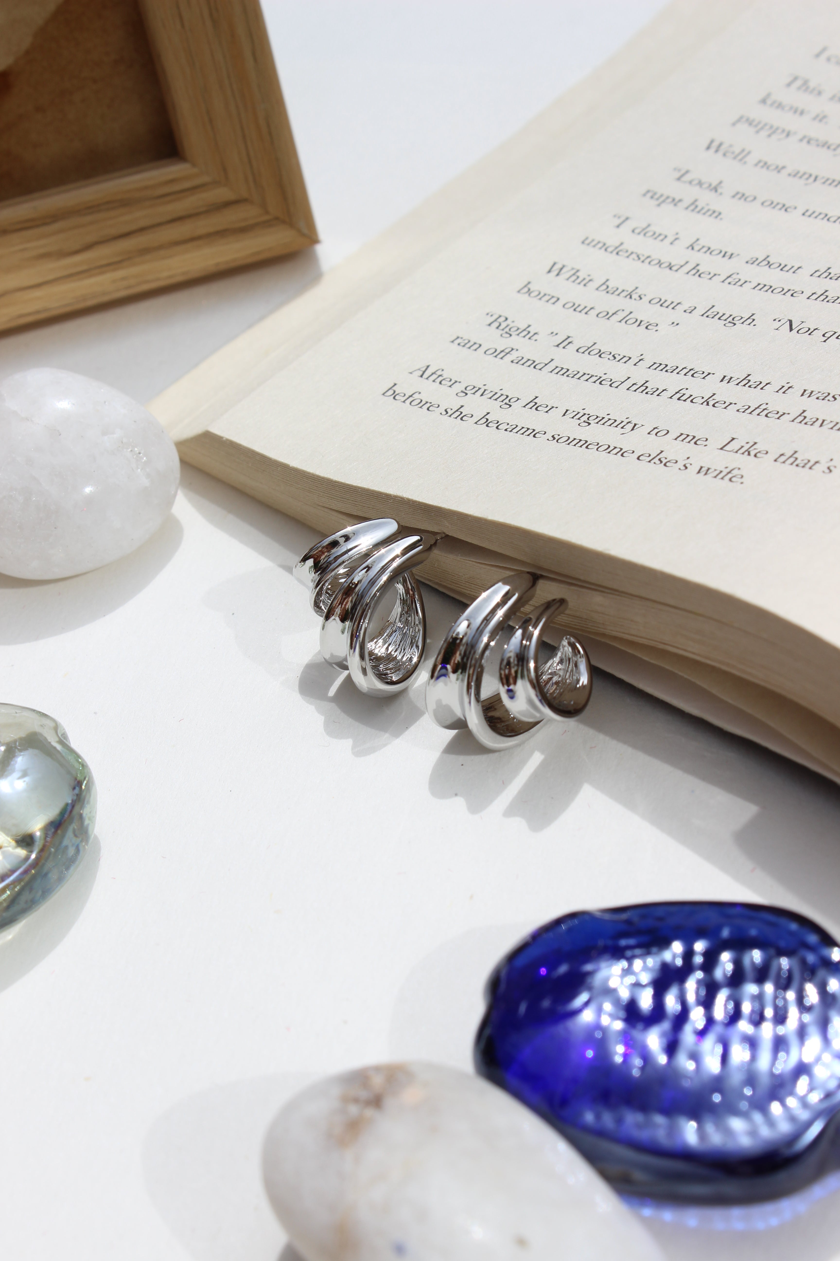 Affordable Winter Hug Earrings displayed on book pages surrounded by sea shells, cozy winter jewellery gift for her, white backdrop