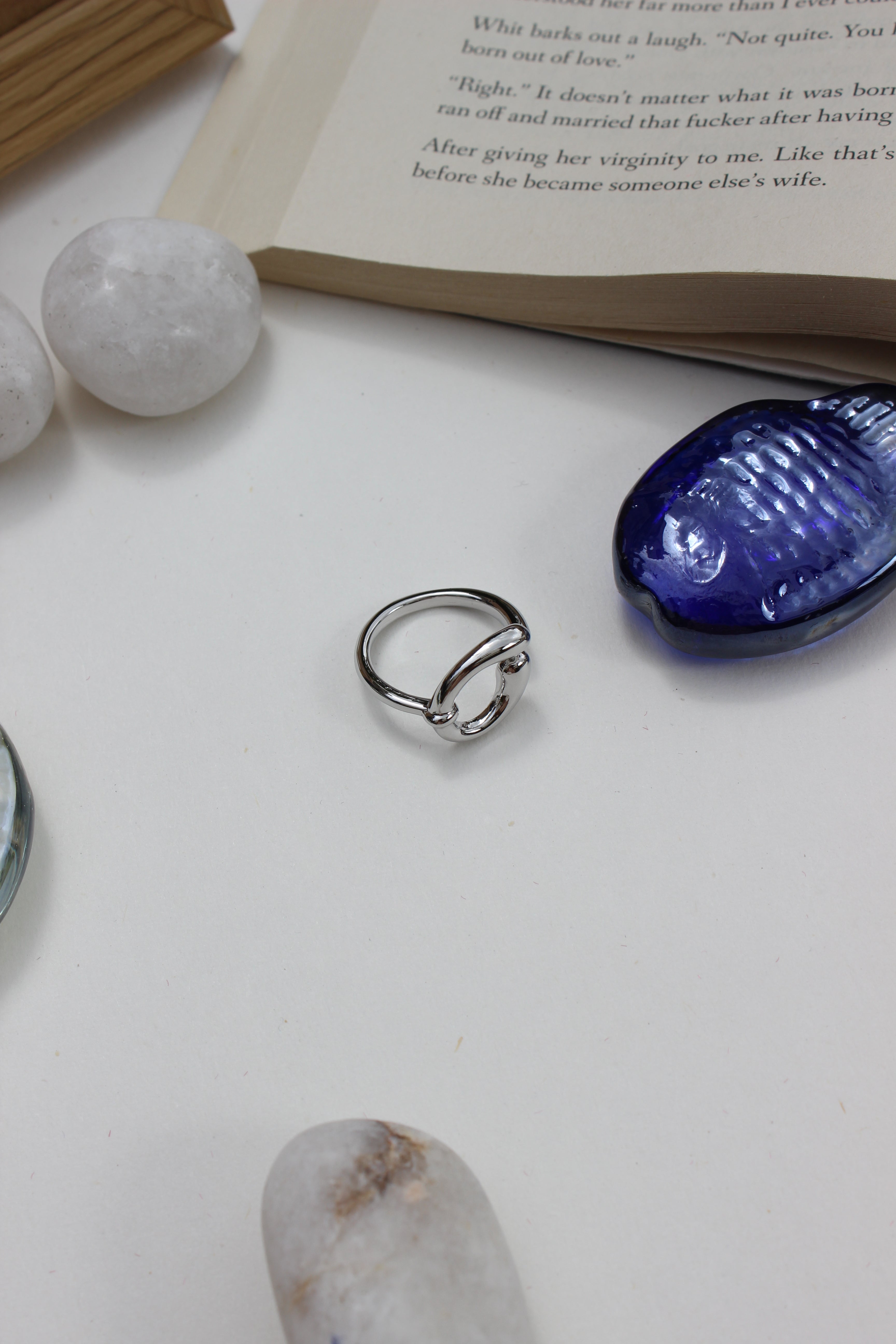 Lunar Trace Ring on a white surface with a blue seashell and book in the background