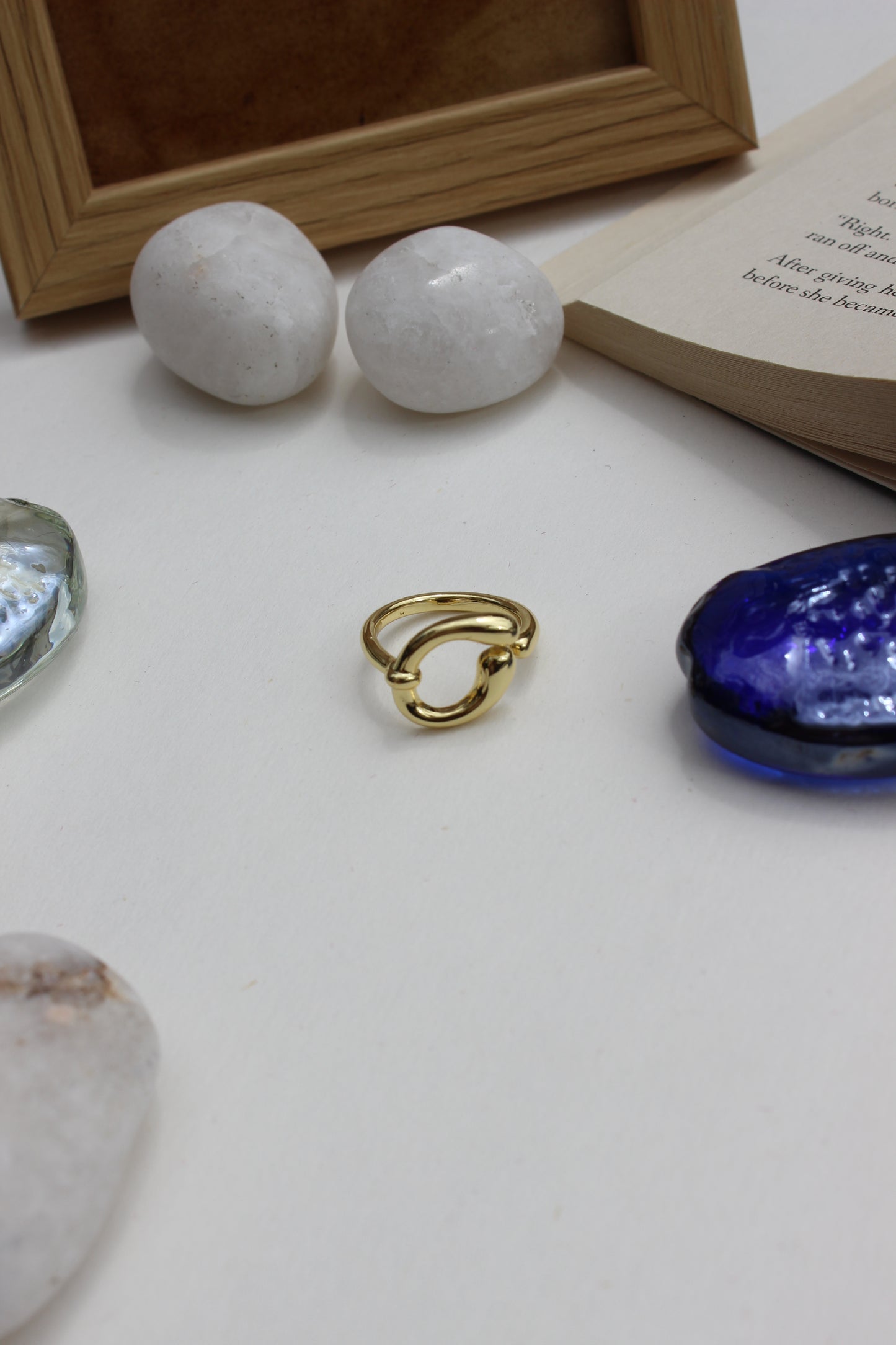 Decorative items including a Warm Loop Ring, blue glass seashell, and two white spherical stones on a light surface