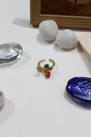 Sweetheart Spritz Ring with green and red stones on a white surface with decorative seashell