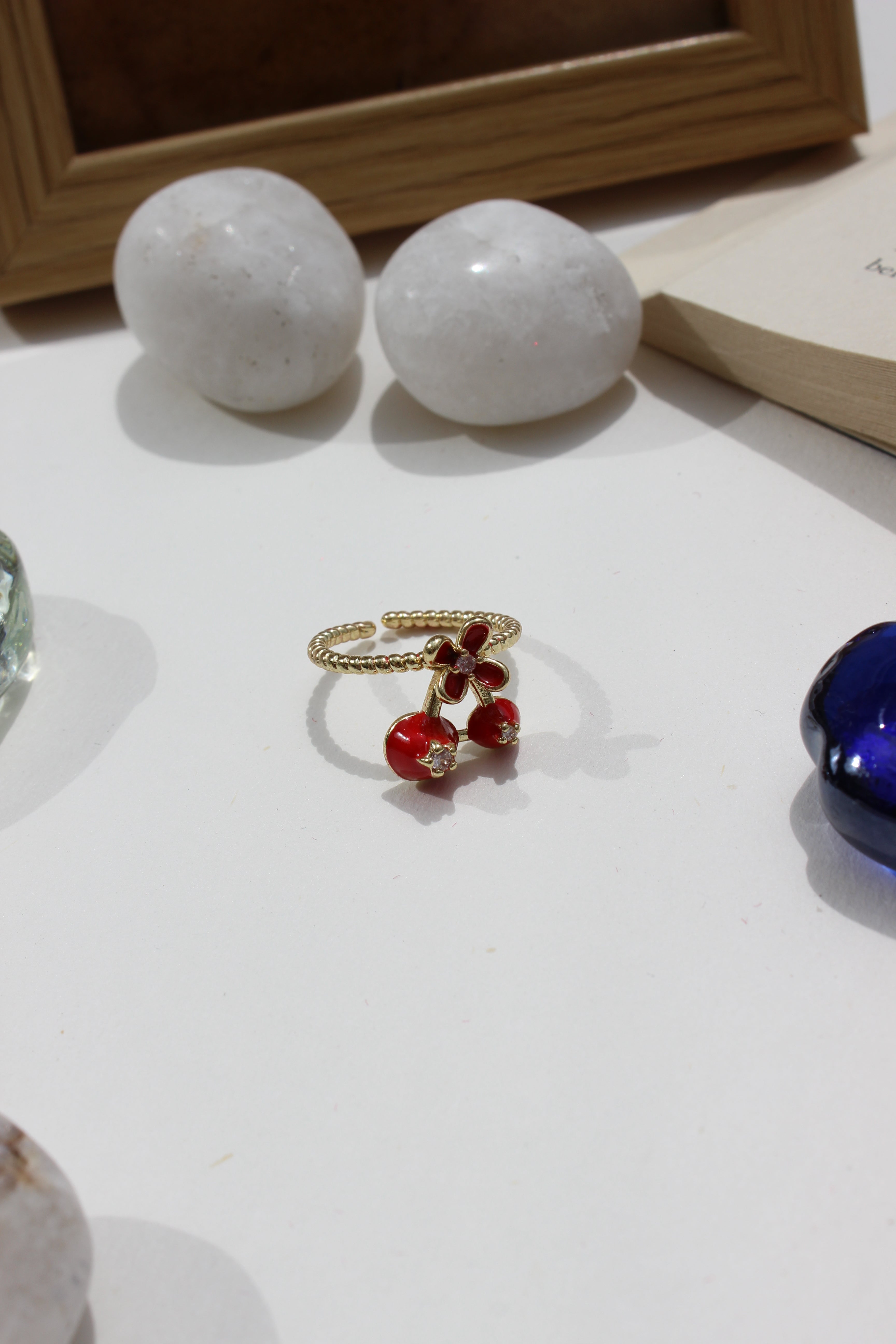 Close-up of a Kiss & Cherry Ring with red beads and gold chain on a white surface