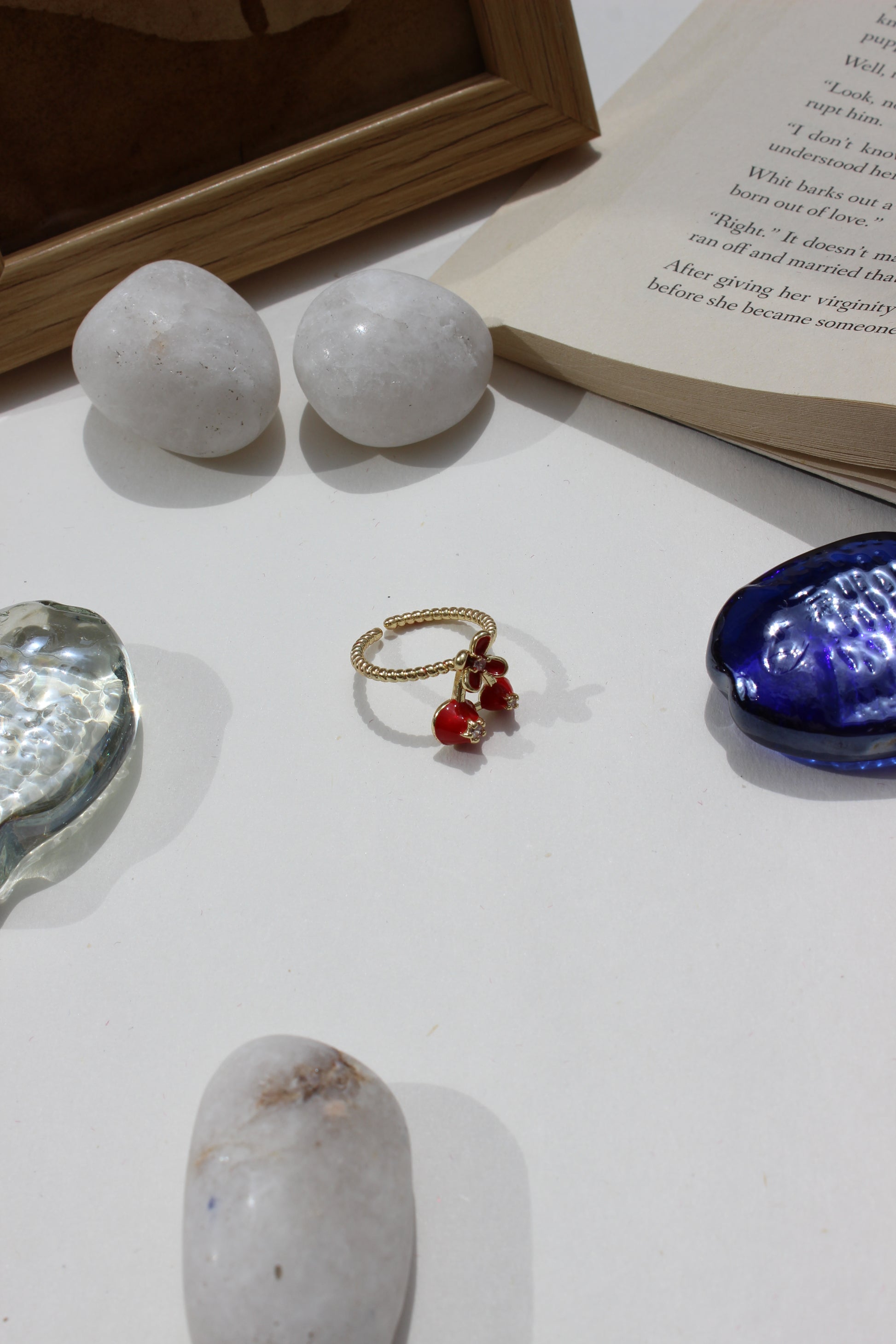 Kiss & Cherry Ring on a white surface with stones and an open book