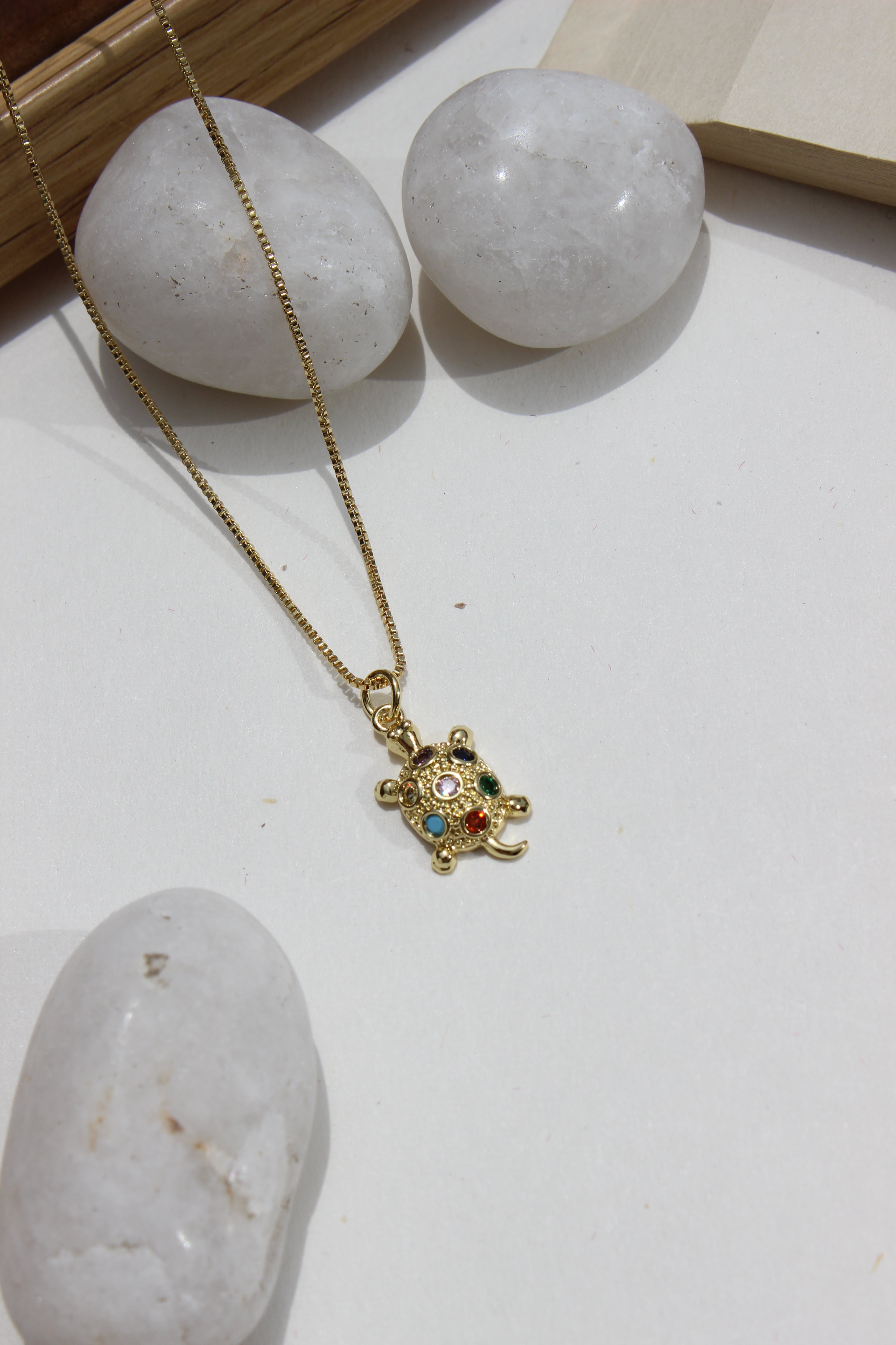 Luck Shell Pendant Necklace on a white surface with stones and wooden frame
