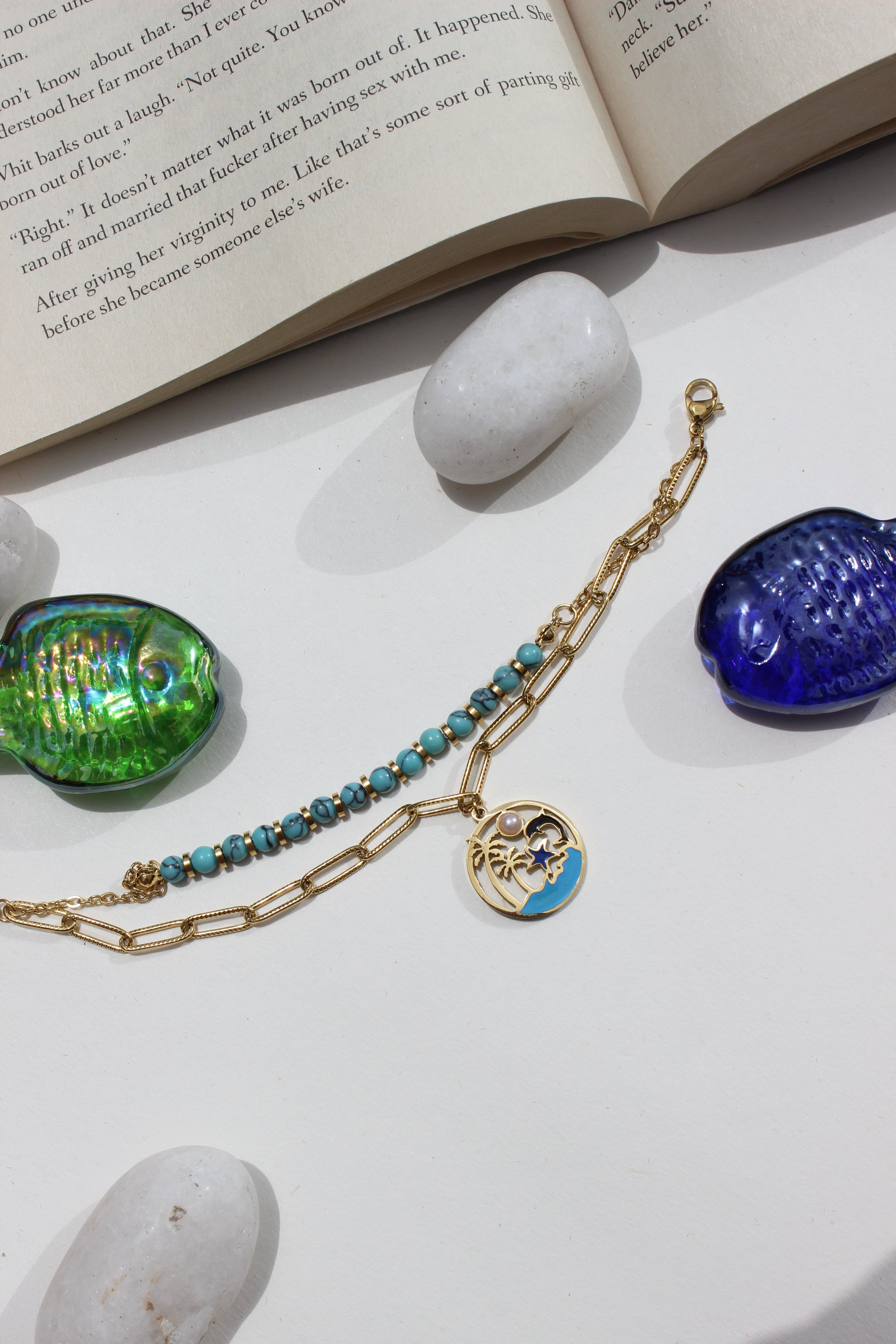 Ocelette Layered Bracelet and blue and green glass beads on a white surface