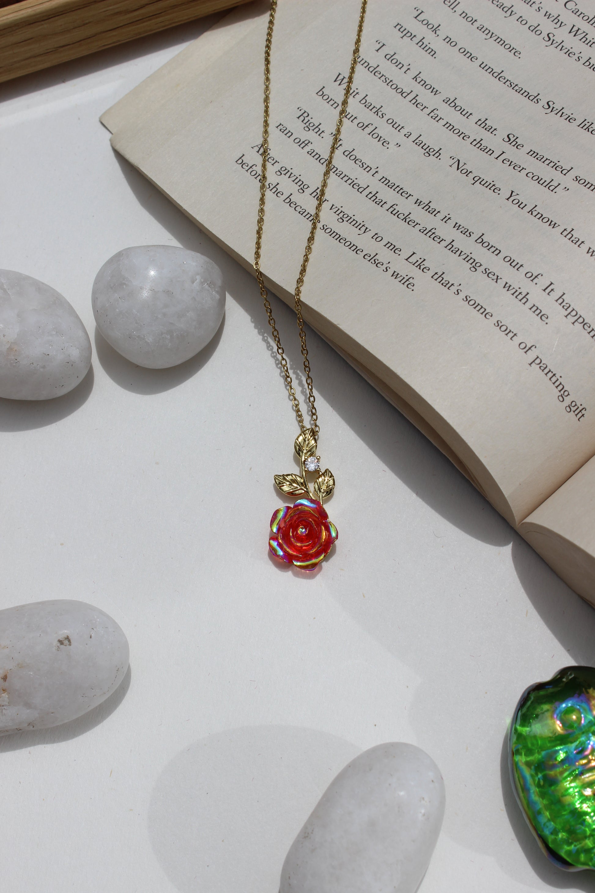 Primrose Dawn Pendant Necklace on a book with stones and a green seashell in the background