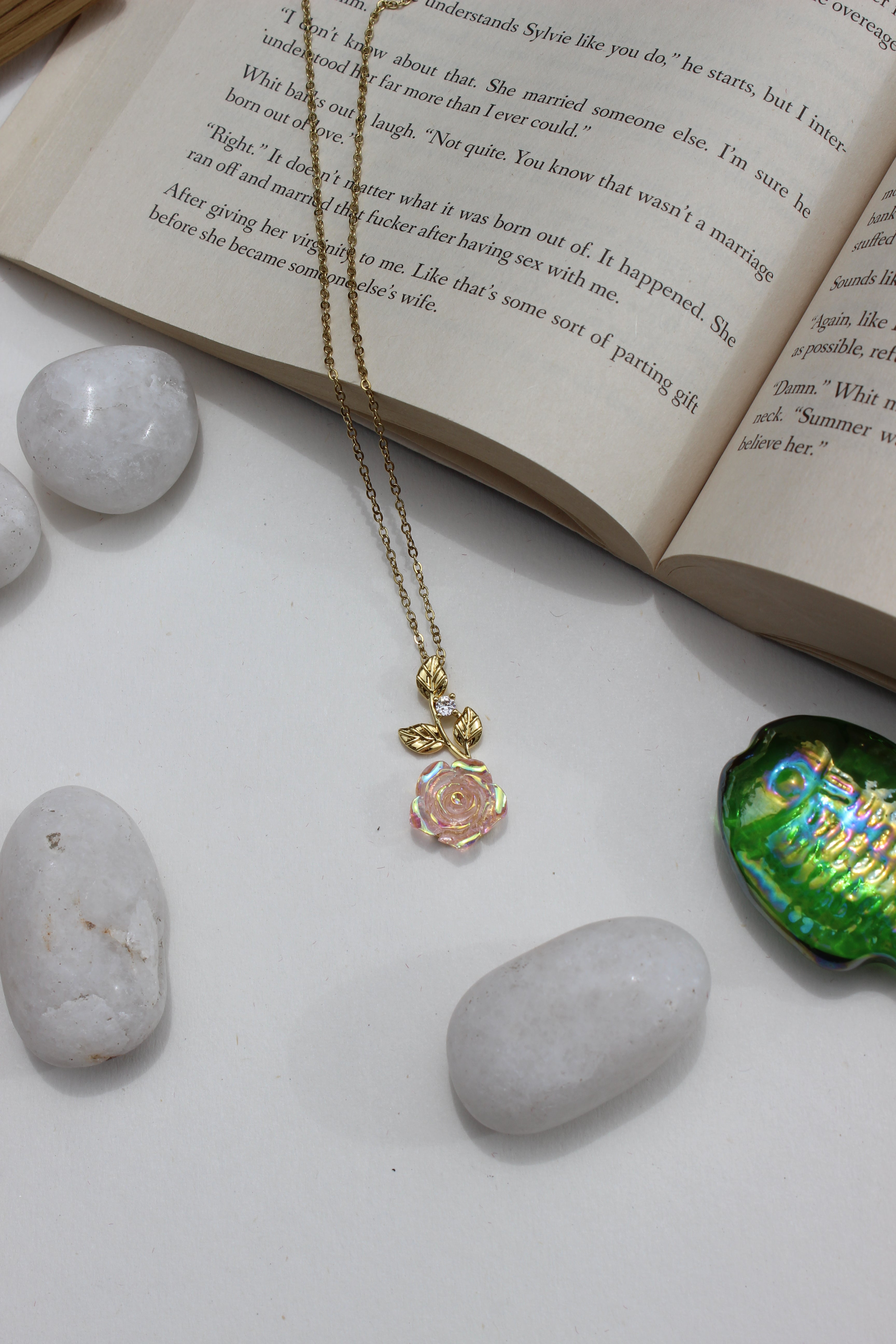Primrose Pendant Necklace on a white surface with stones and an open book