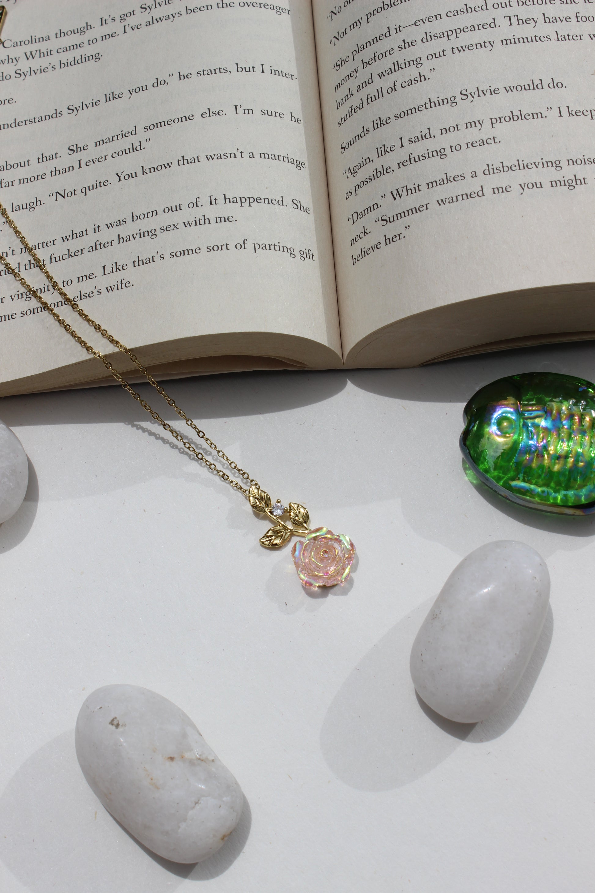 Primrose Pendant Necklace on an open book next to pebbles