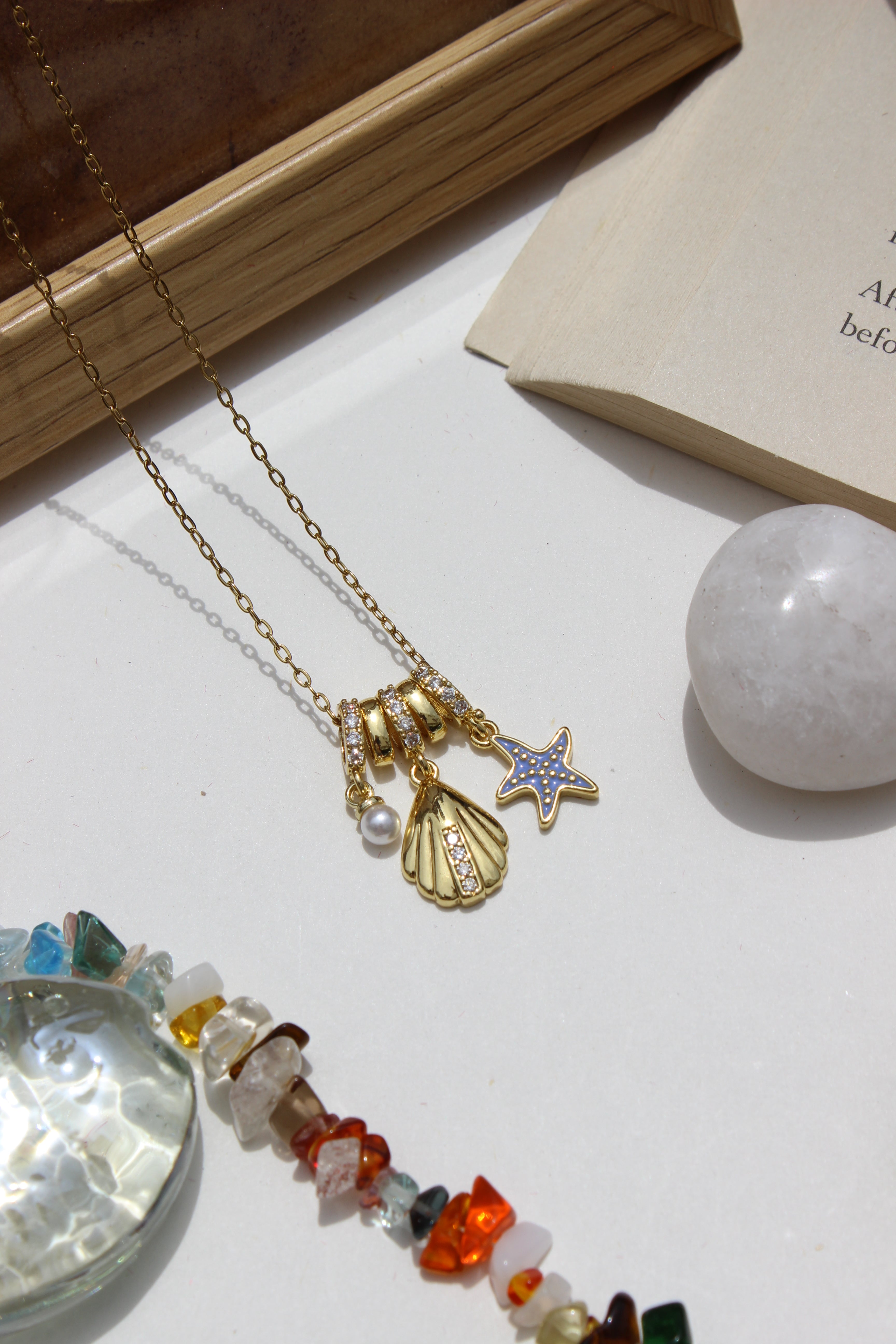Mermaid Keepsake Charms Pendant Necklace on a white surface with a book and crystal ball in the background