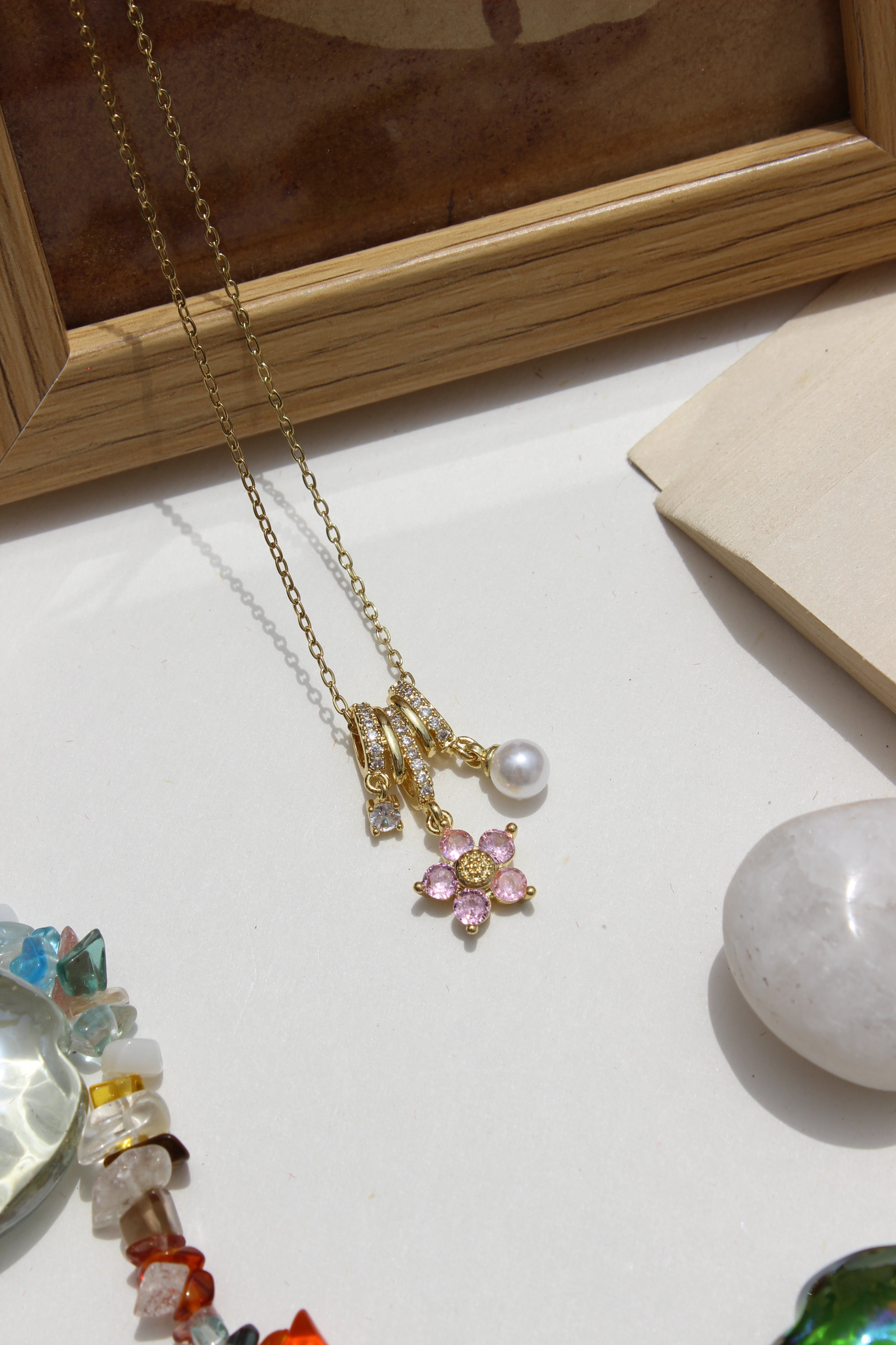 Jewelry including a Twinkle Flora Charms Pendant Necklace on a light surface with a wooden frame