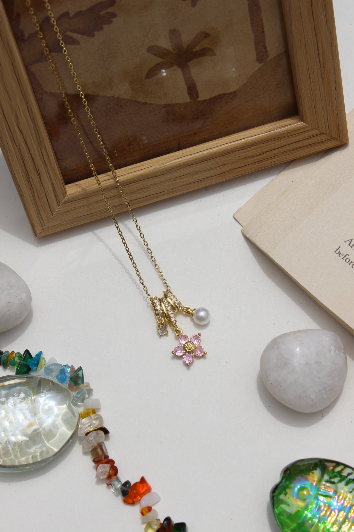 Twinkle Flora Charms Pendant Necklace on a white surface with a wooden frame and decorative stones