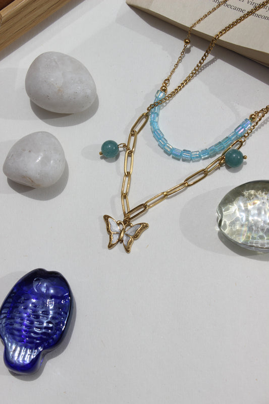 Butterbead Layered Necklace on a white surface with stones and a blue fish-shaped seashell