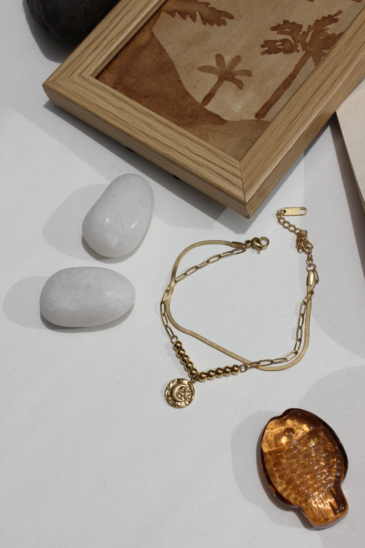 Golden Phase Layered Bracelet on a white surface with stones and a wooden box