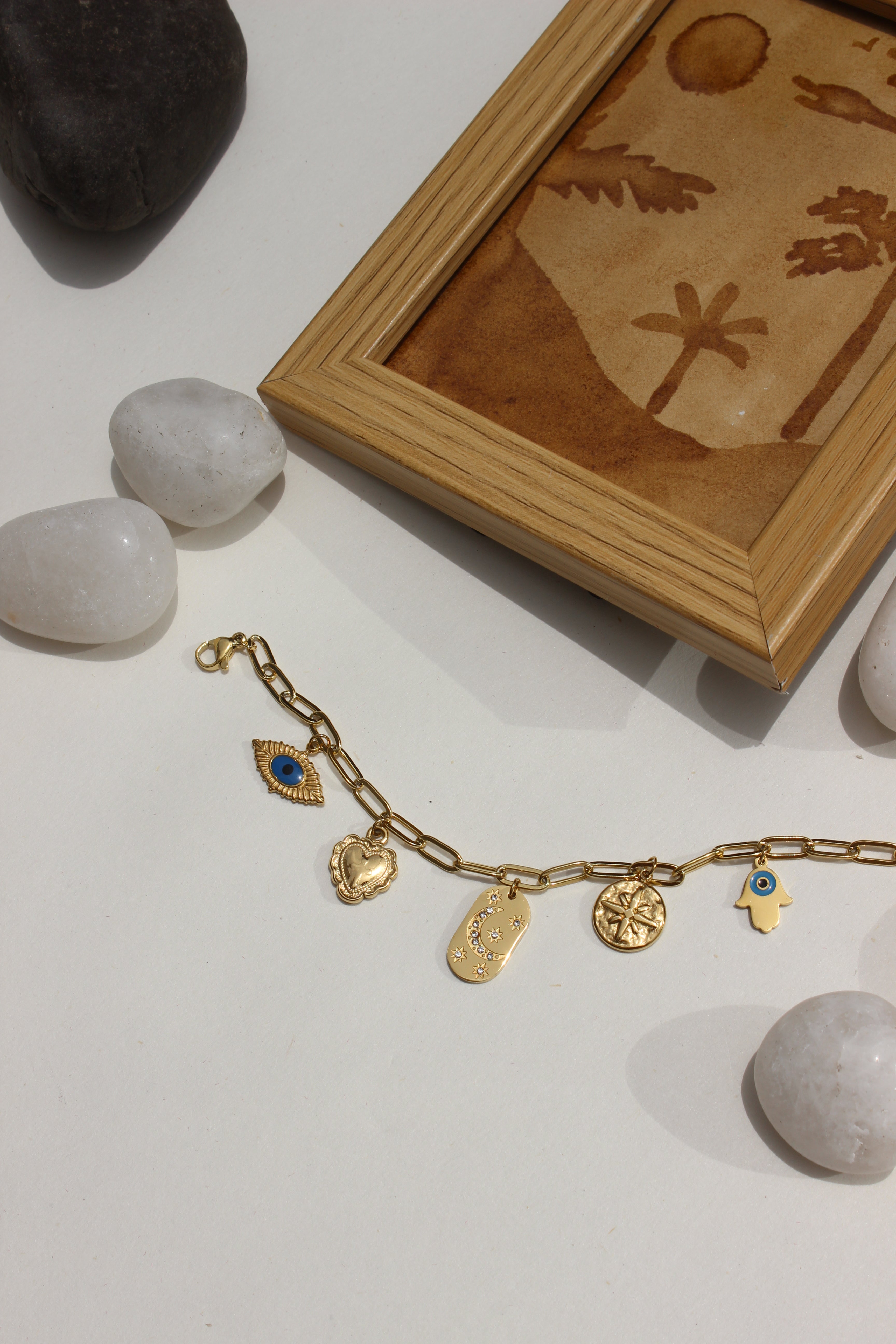 Whispershield Charms Bracelet with charms on a light surface next to a wooden box and stones
