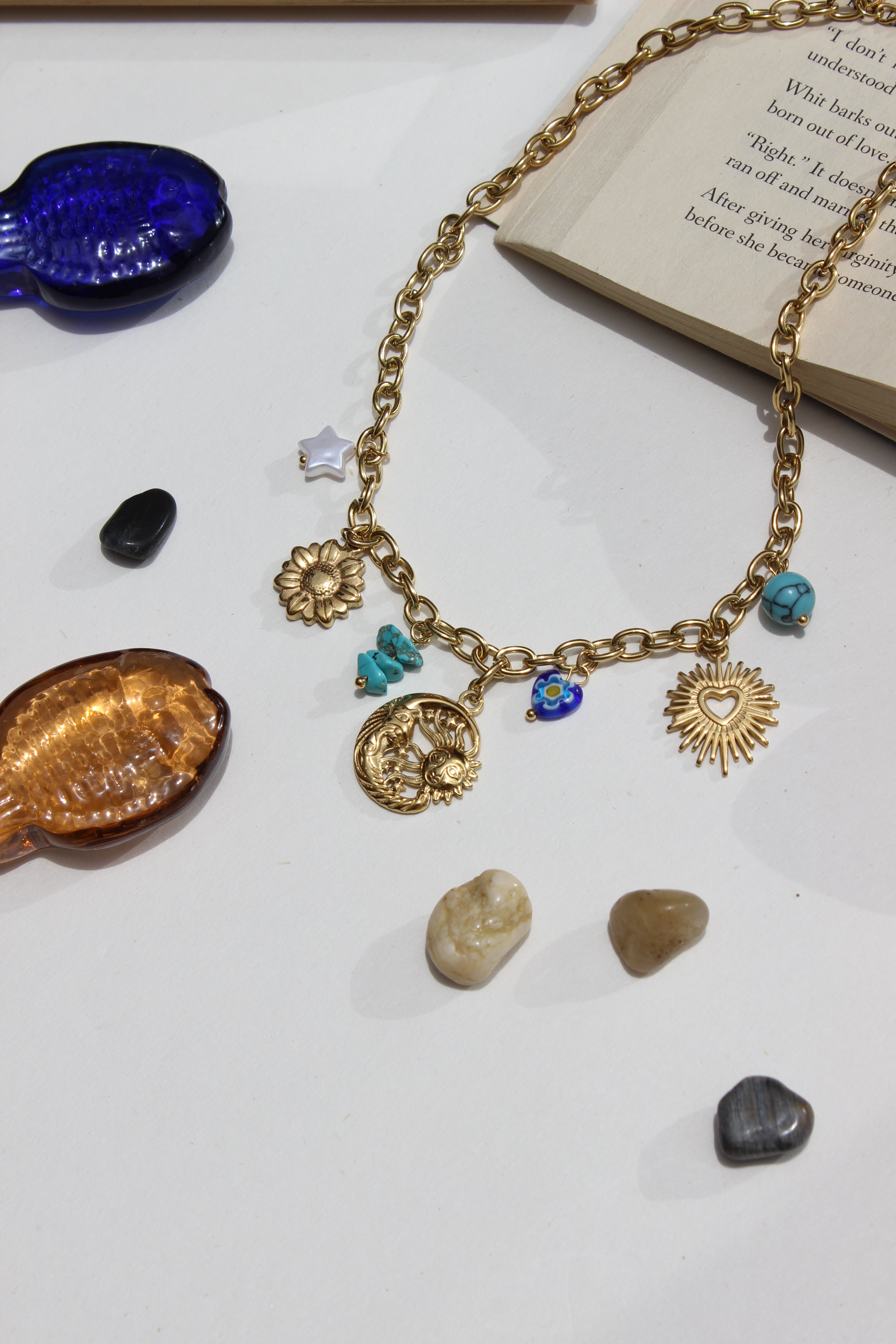Solaris & Selene Charms Necklace with charms on a white surface with seashells and a book