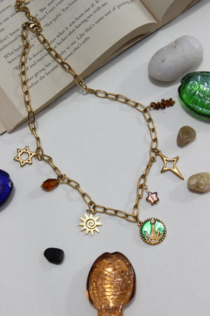 Amberjoy Charms Necklace on a white surface with stones and an open book