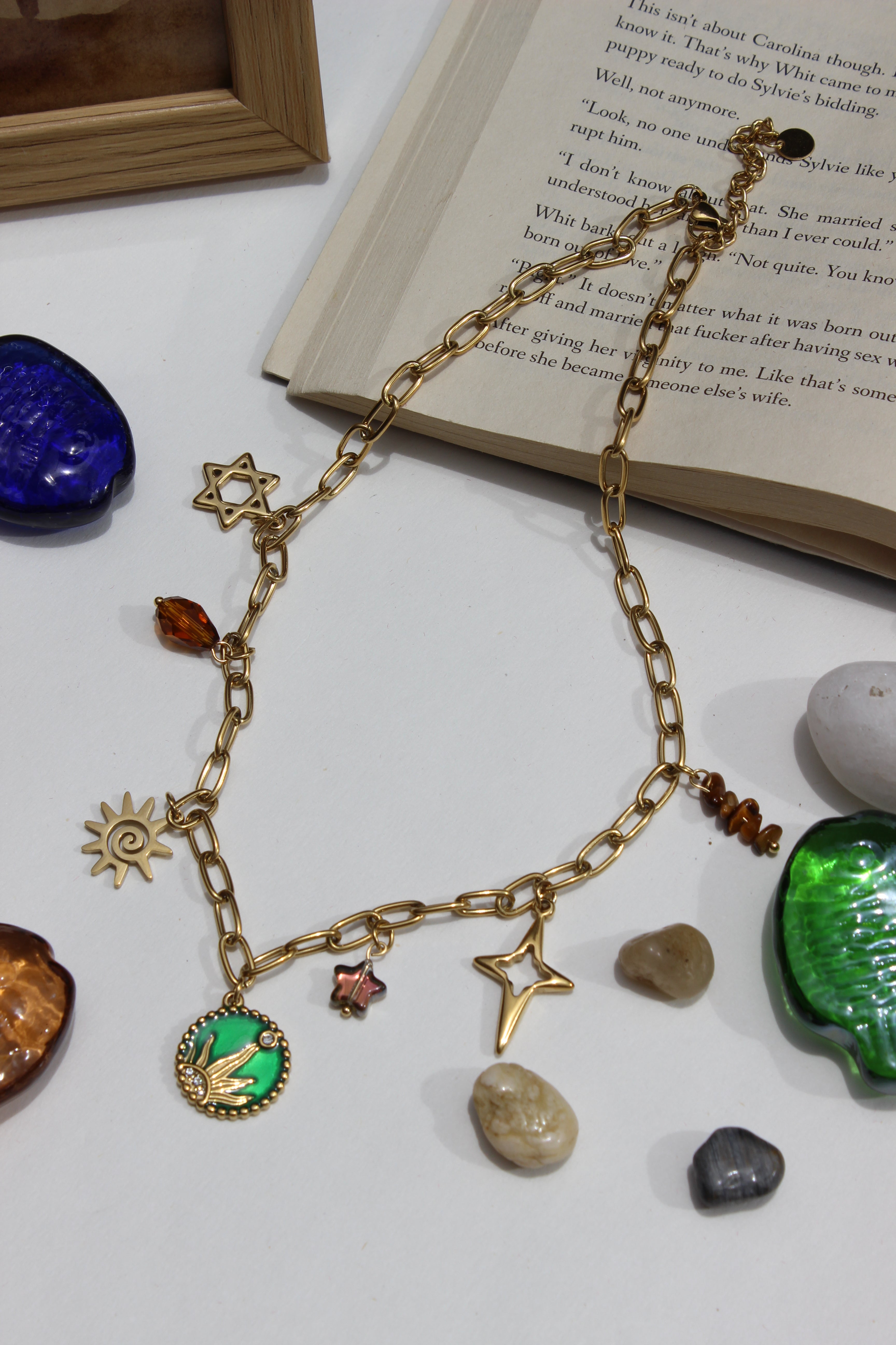Amberjoy Charms Necklace on a white surface with a book and stones