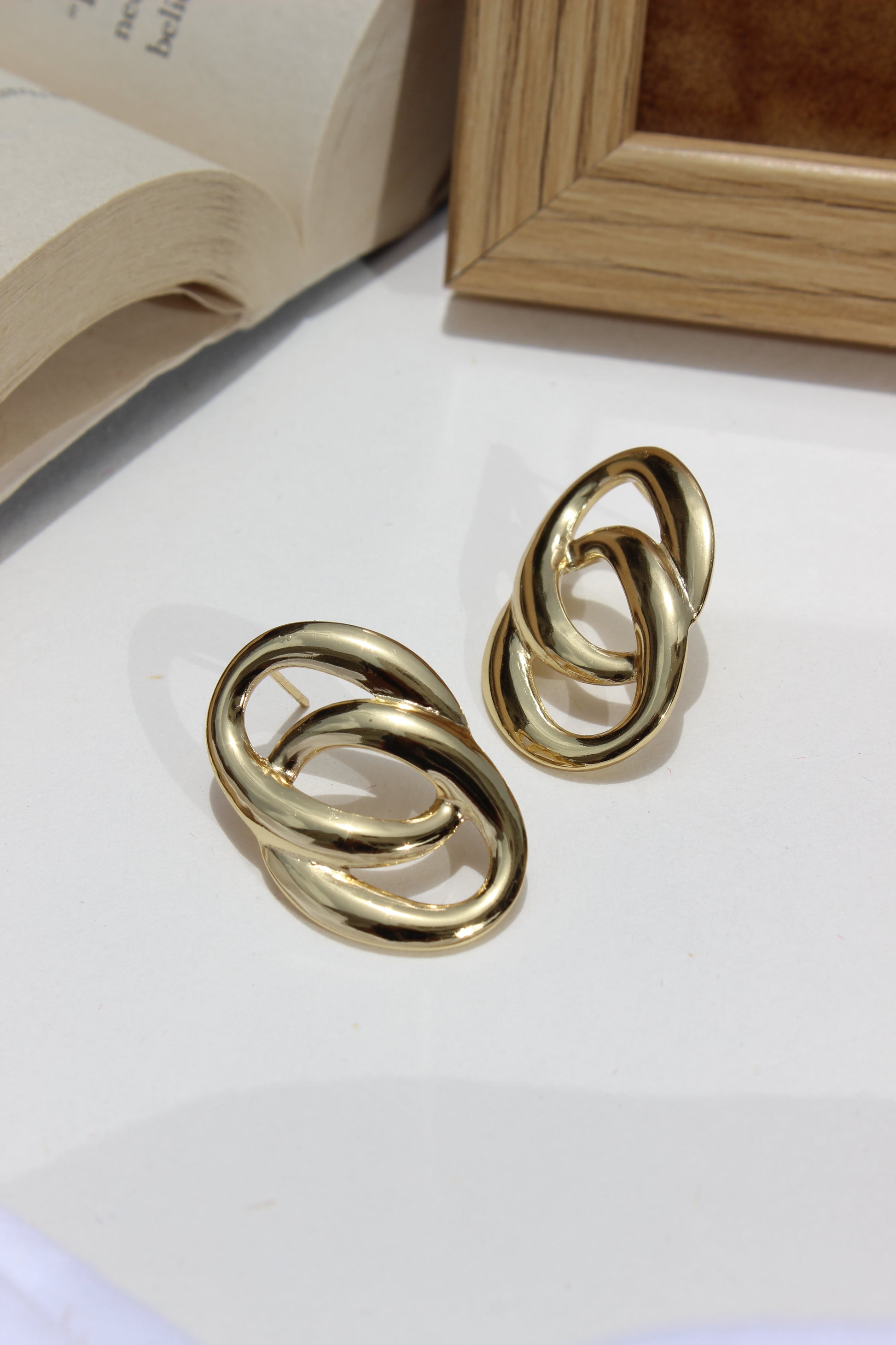 Daily Gleam Earrings on a light surface with a wooden frame in the background