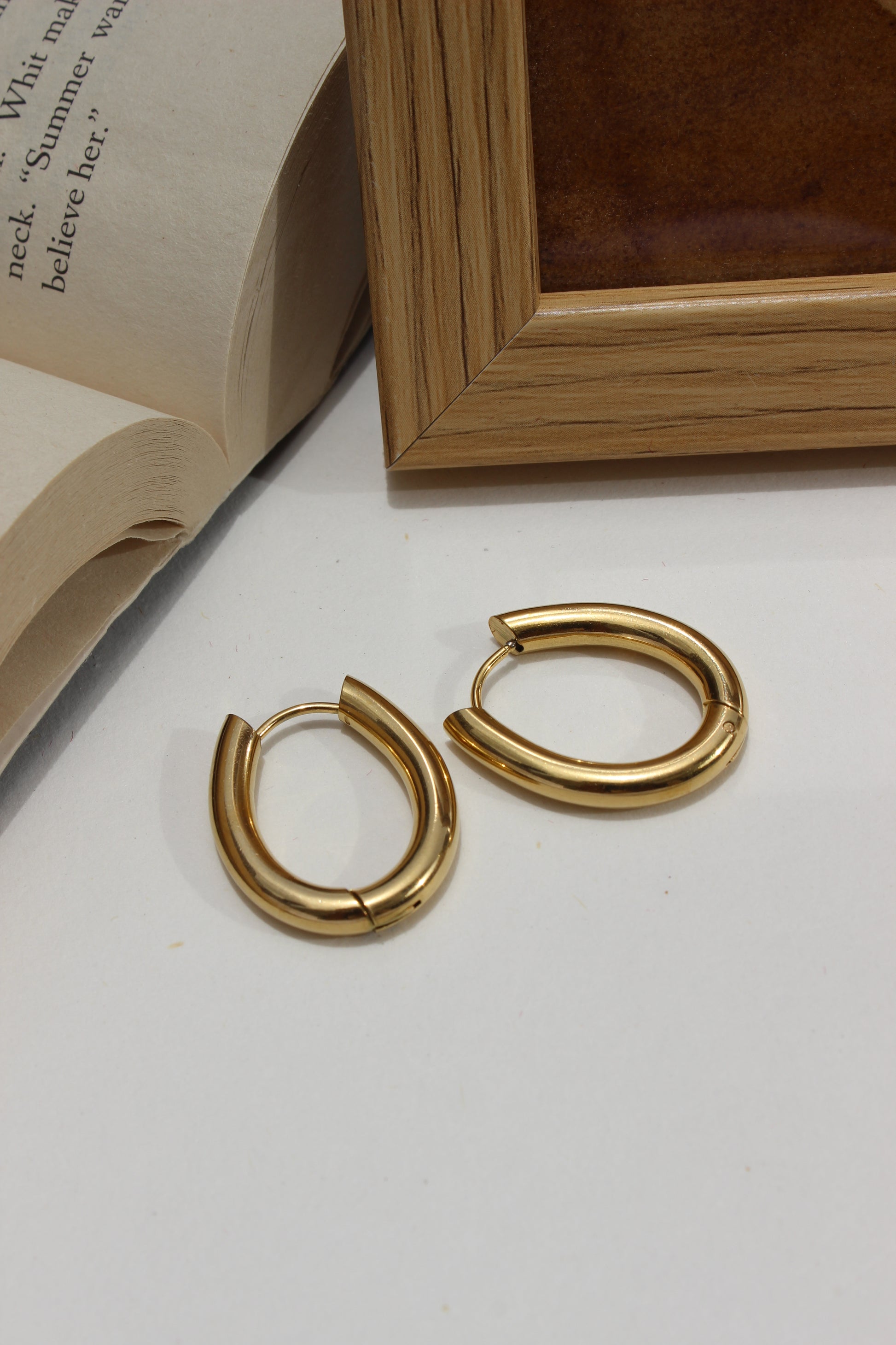 Aurume Earrings on a white surface with a wooden frame and book corner in the background